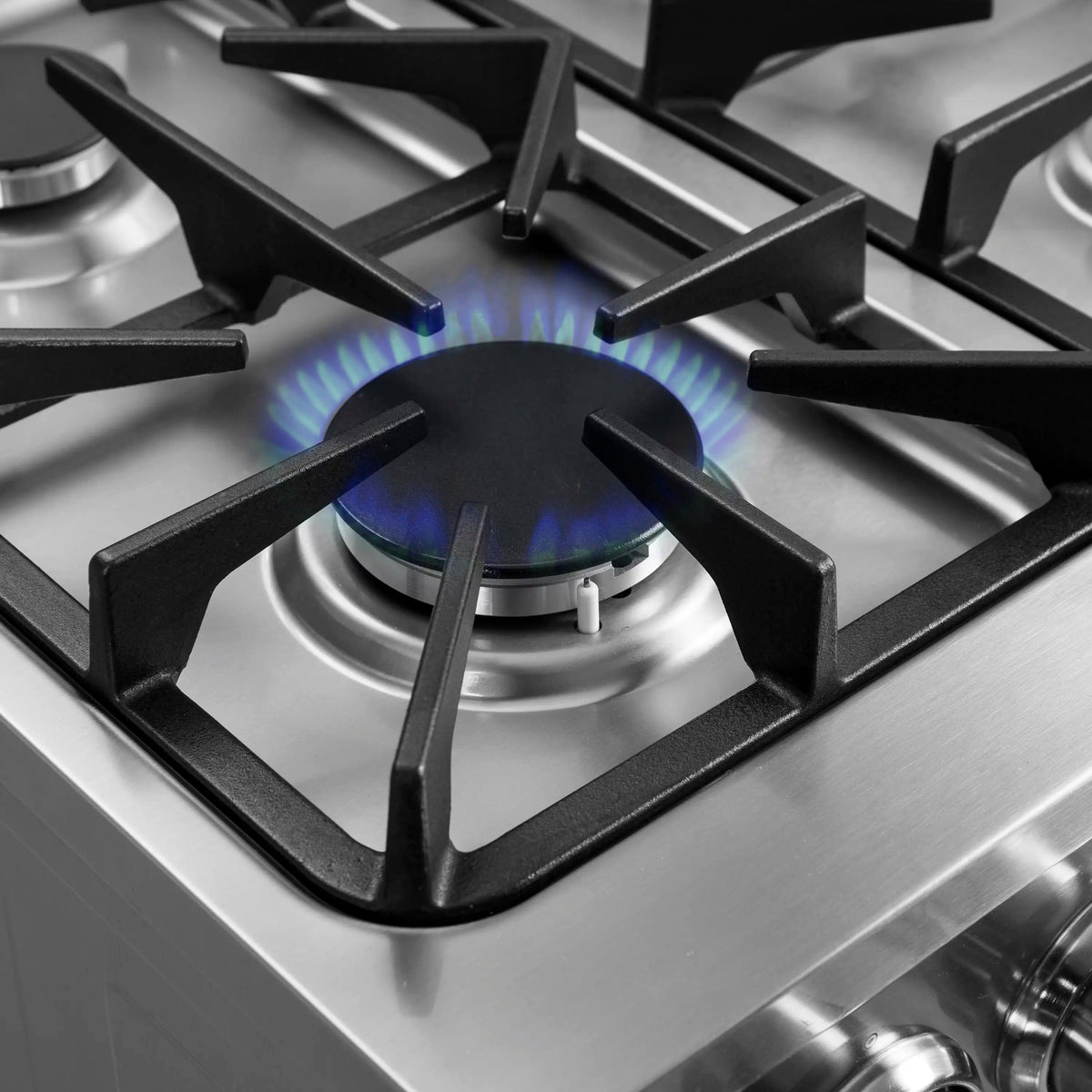Lit gas burner on stainless steel cooktop with black burner grate and blue flame.