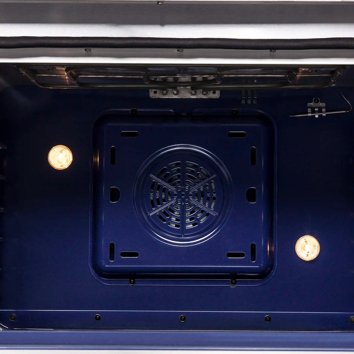 Oven cavity view with round convection fan cover and two lit side lamps, blue interior.