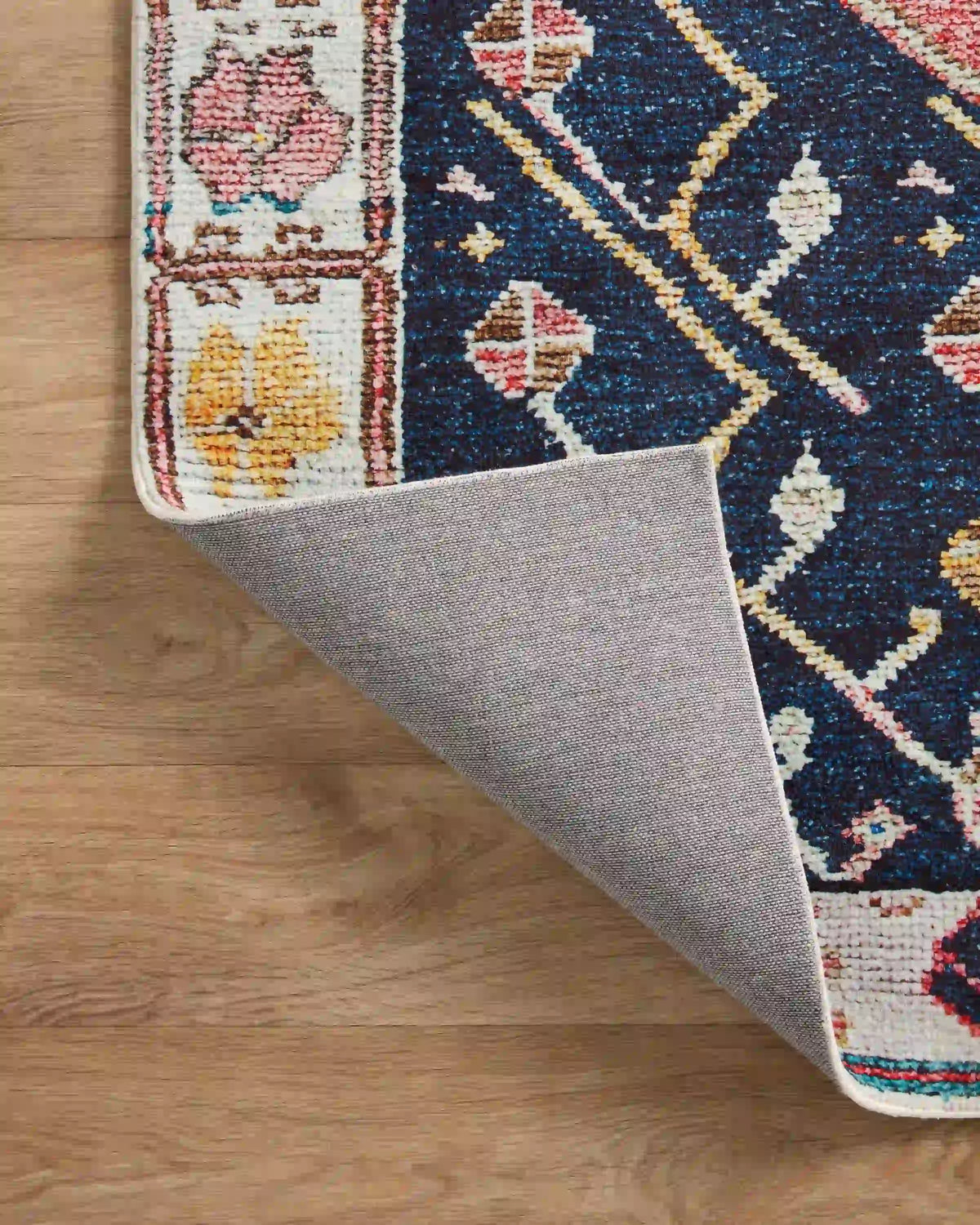 Rug edge with gray backing showing beneath a multicolor navy and rust design