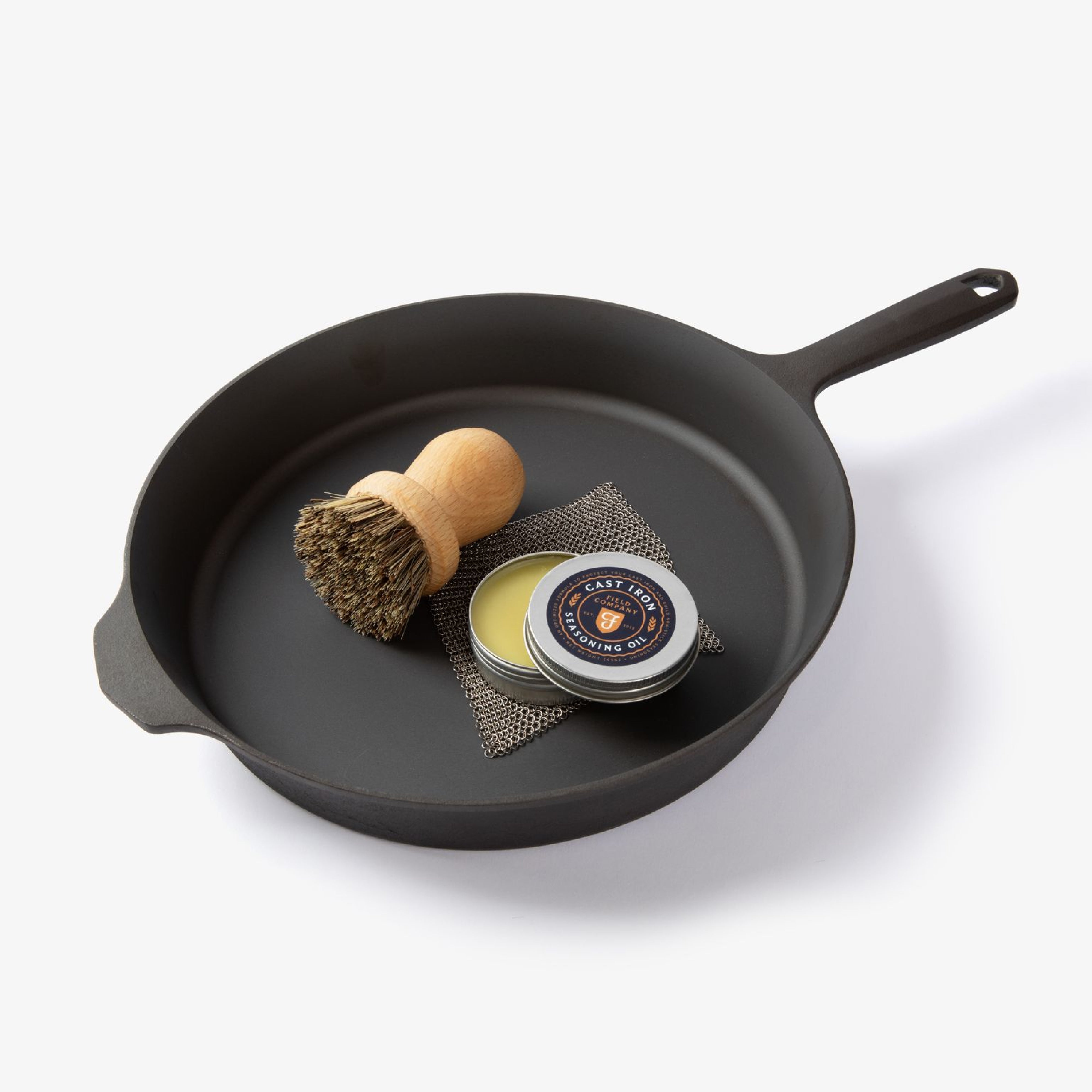 Dark cast-iron skillet with scrubber brush and seasoning tin inside