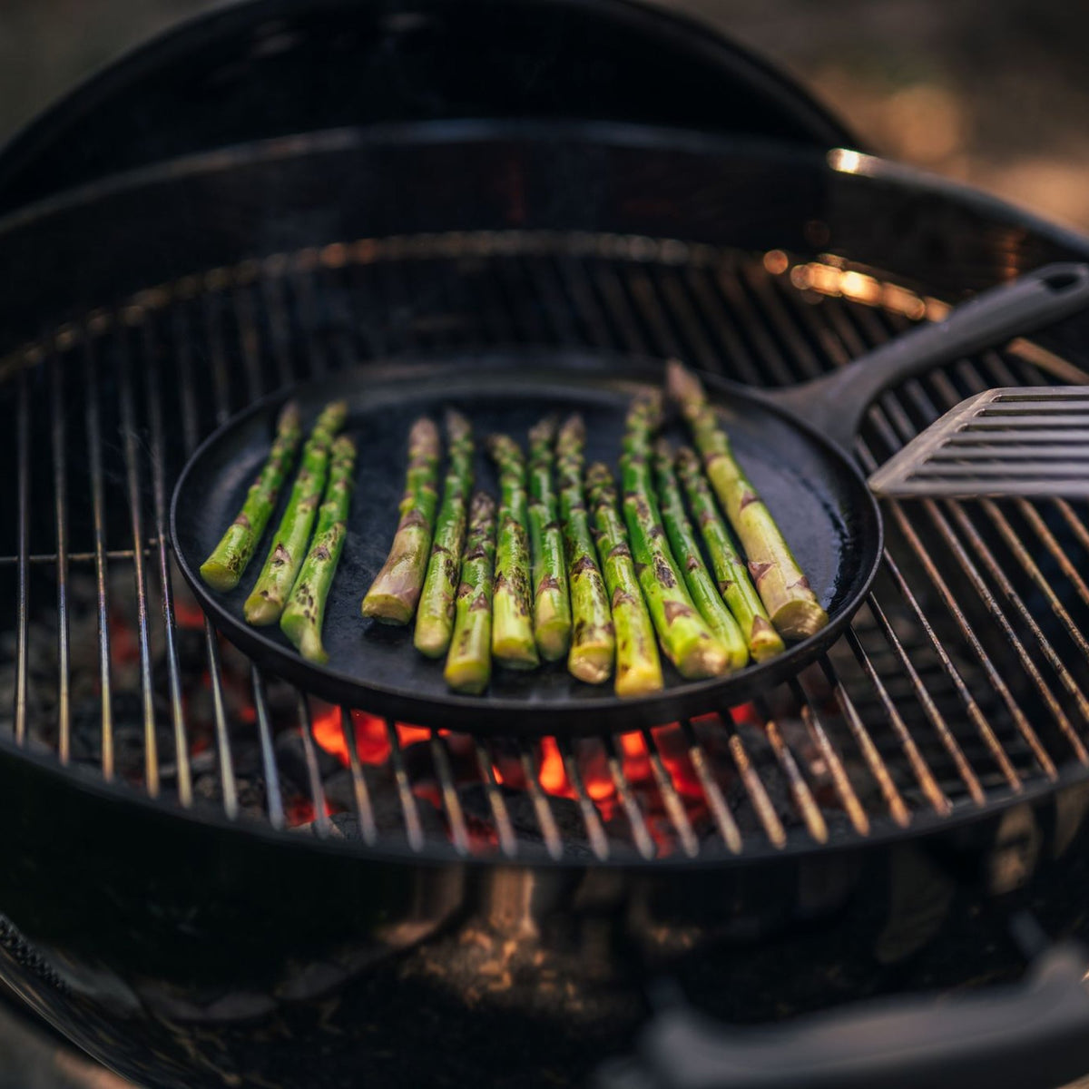 Round cast iron griddle on grill with asparagus spears