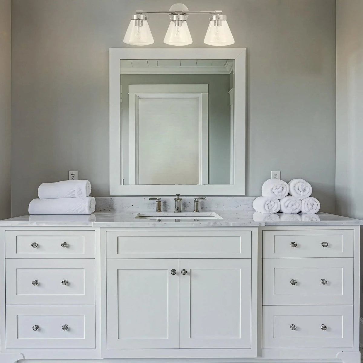 Brush nickel 3-light vanity light with clear glass shades and lit exposed bulbs
