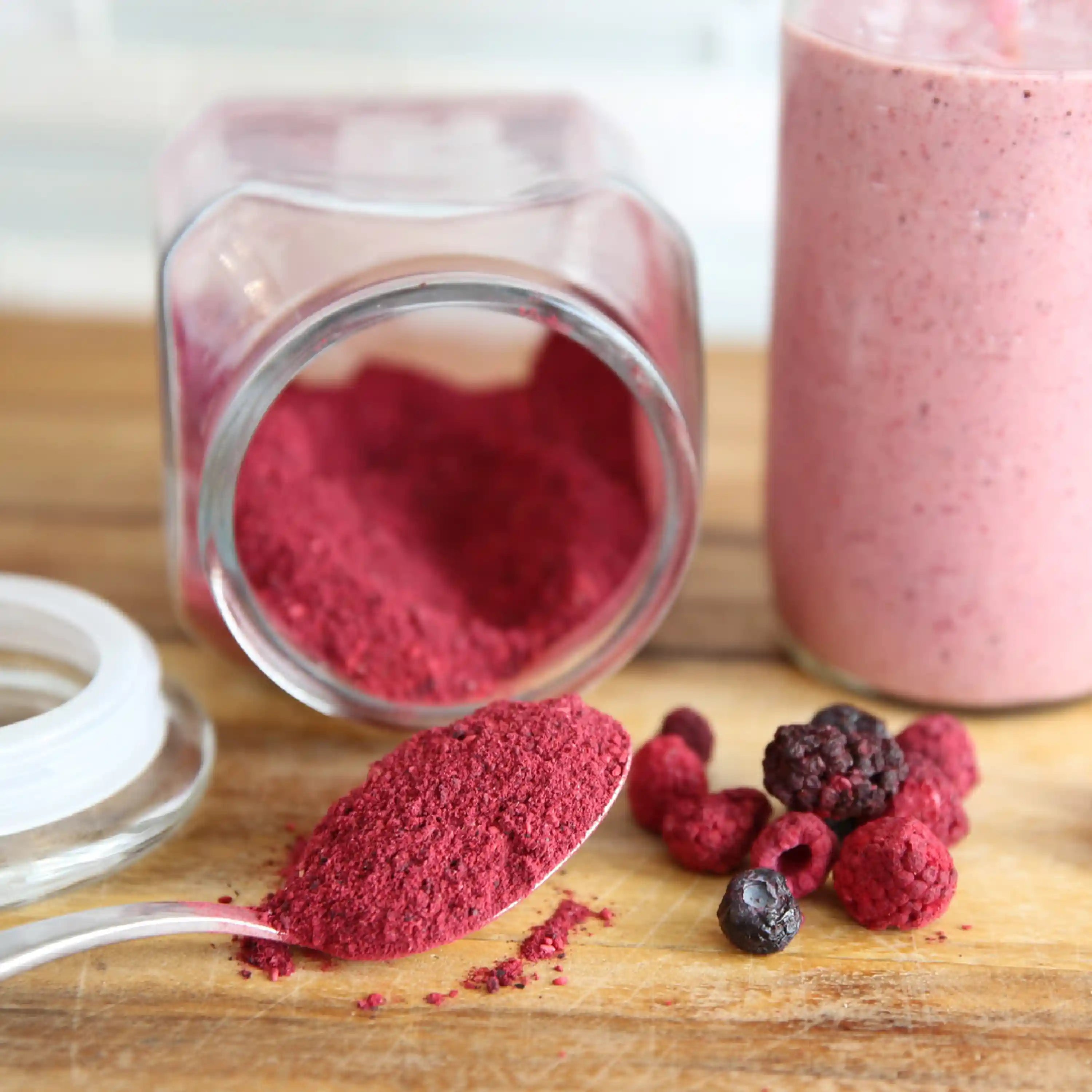 Jar of freeze-dried berry powder with fruit pieces on a wooden surface
