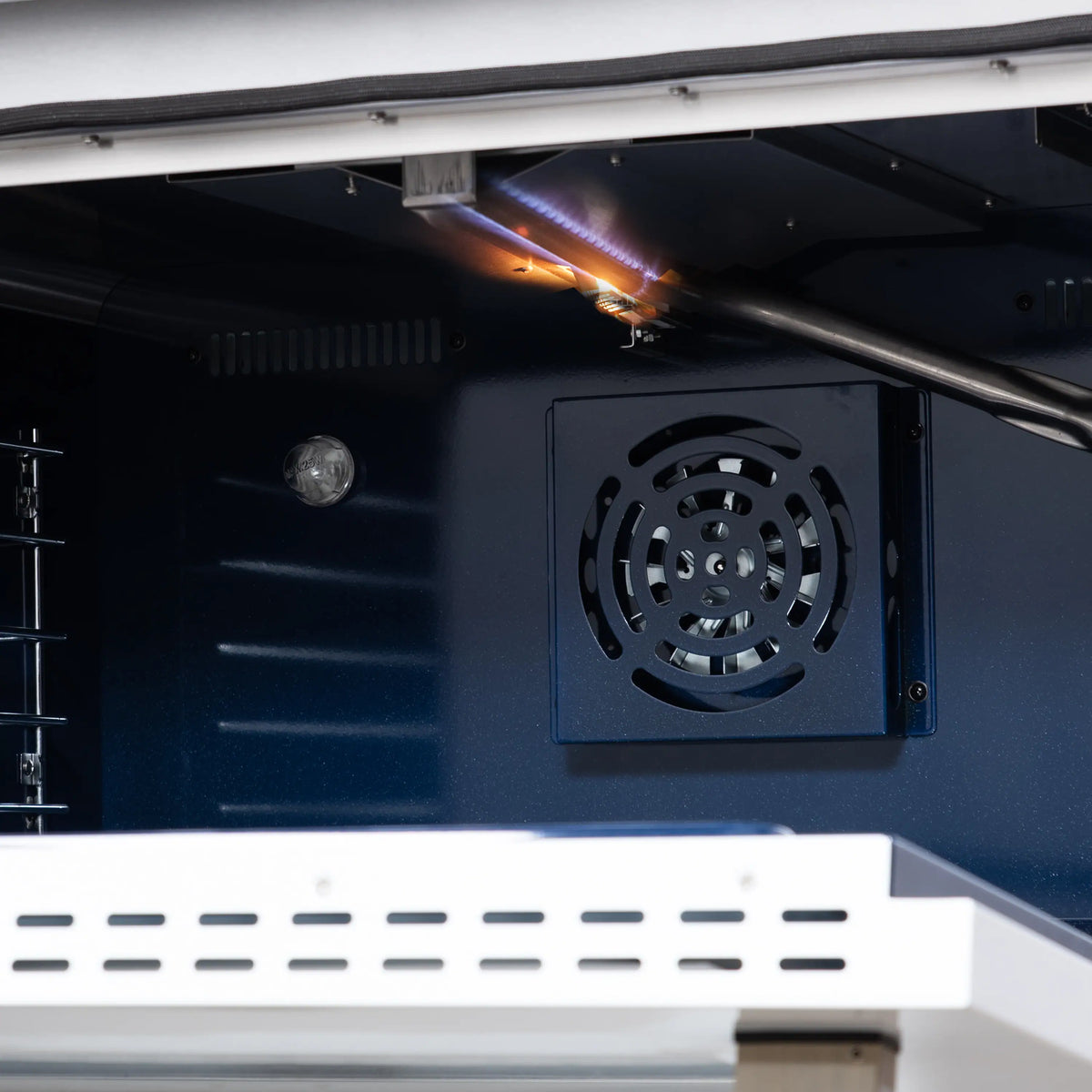 Oven interior with burner flame under broiler, fan vent grille on back wall