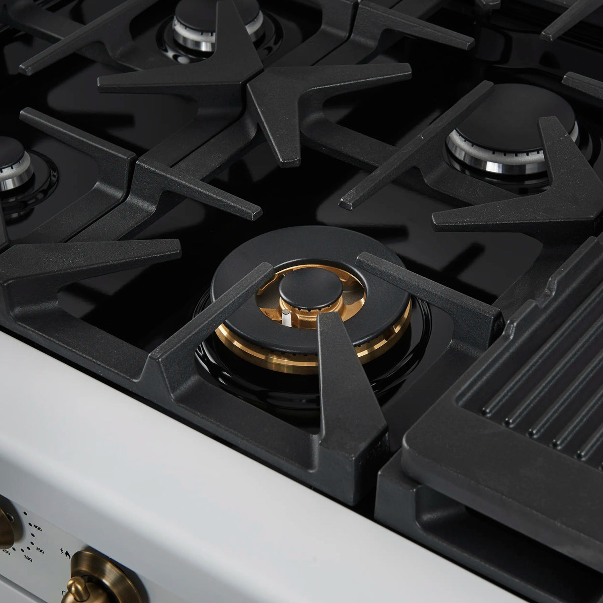Black gas cooktop grate with gold burner head and white range trim.