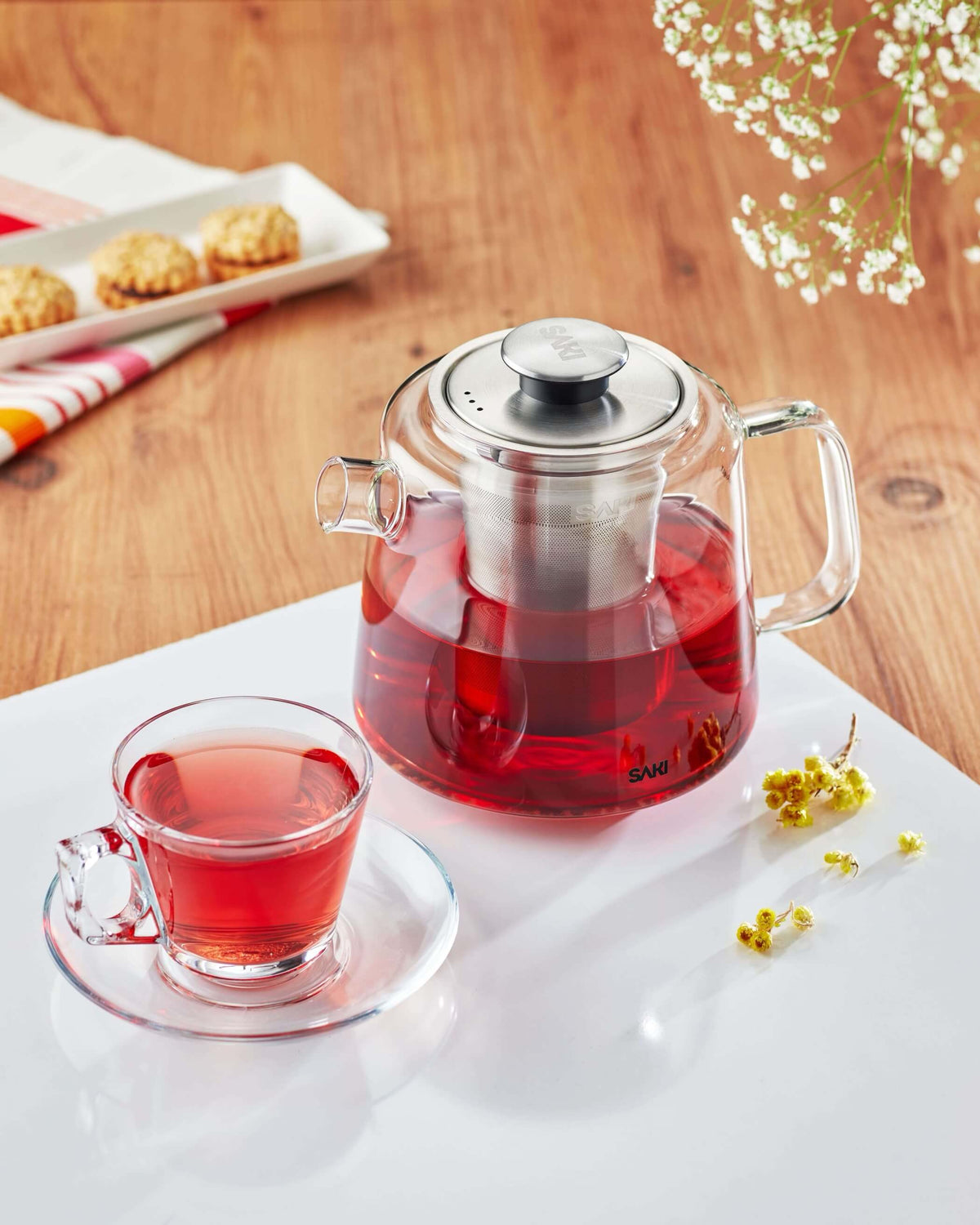 Stainless electric tea maker with glass teapot and red tea, served with cups.