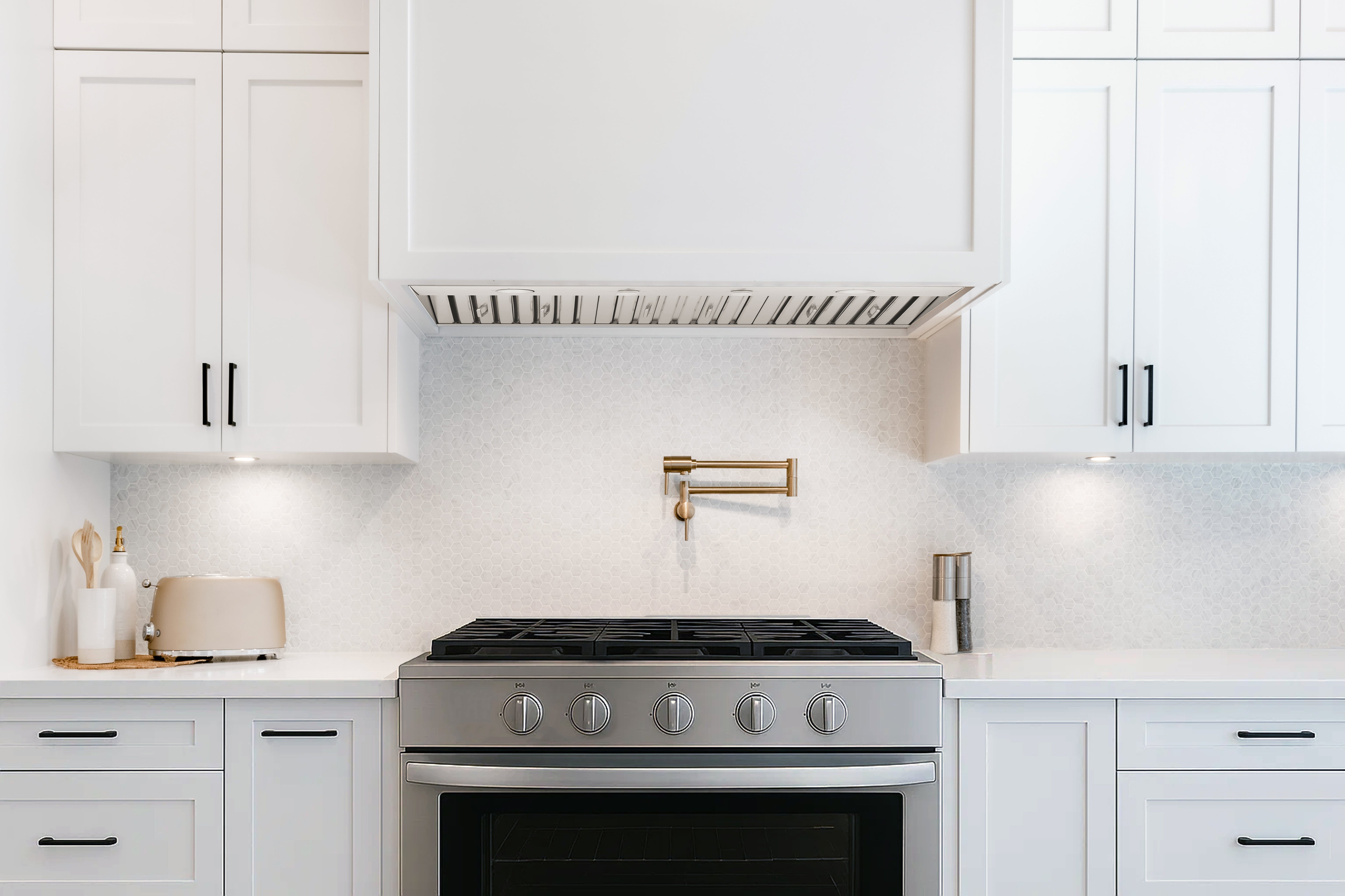 Stainless steel range hood installed above a gas cooktop with four front control knobs.