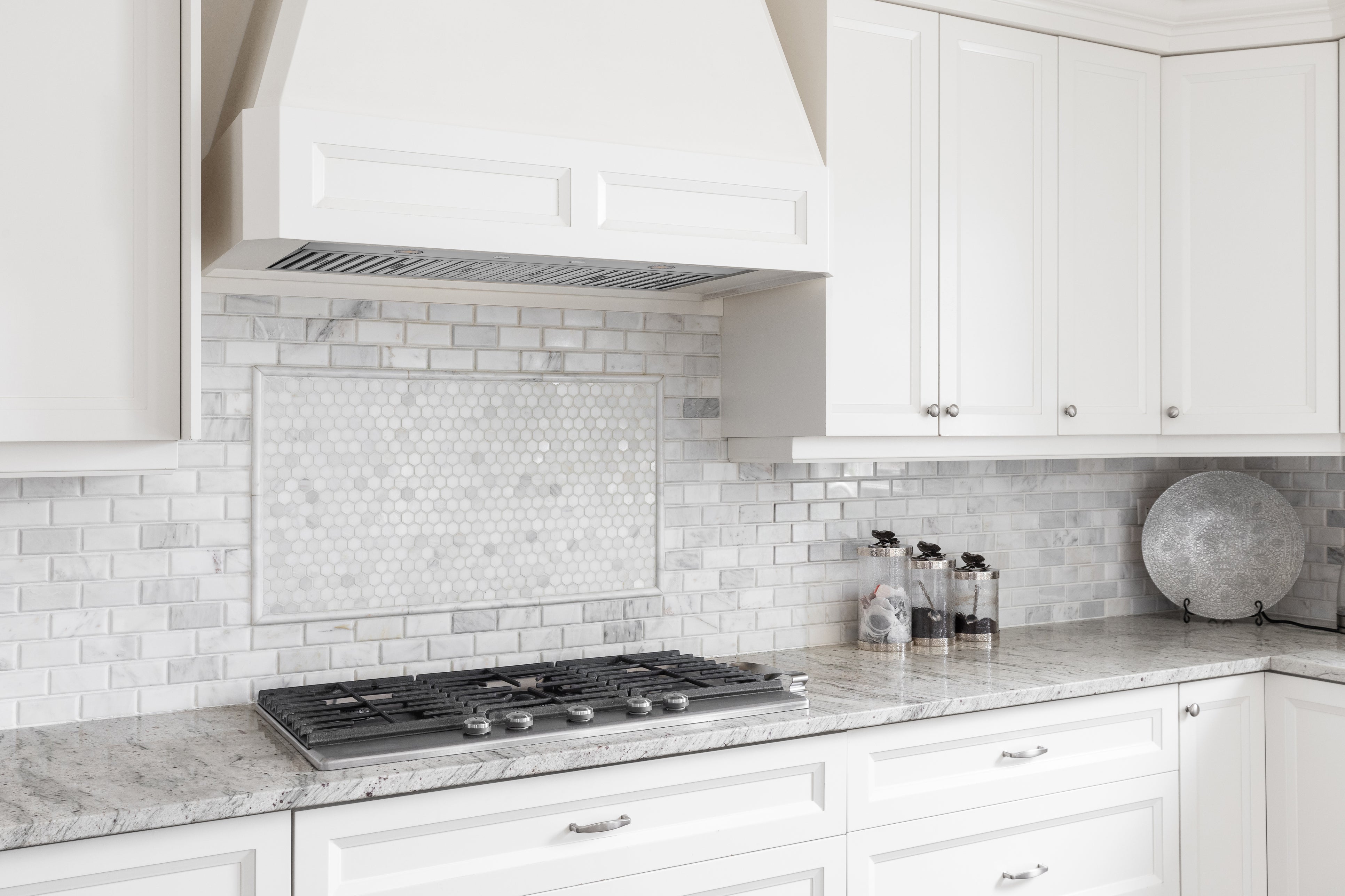 Stainless steel range hood over a cooktop, with vent canopy and backsplash area visible.