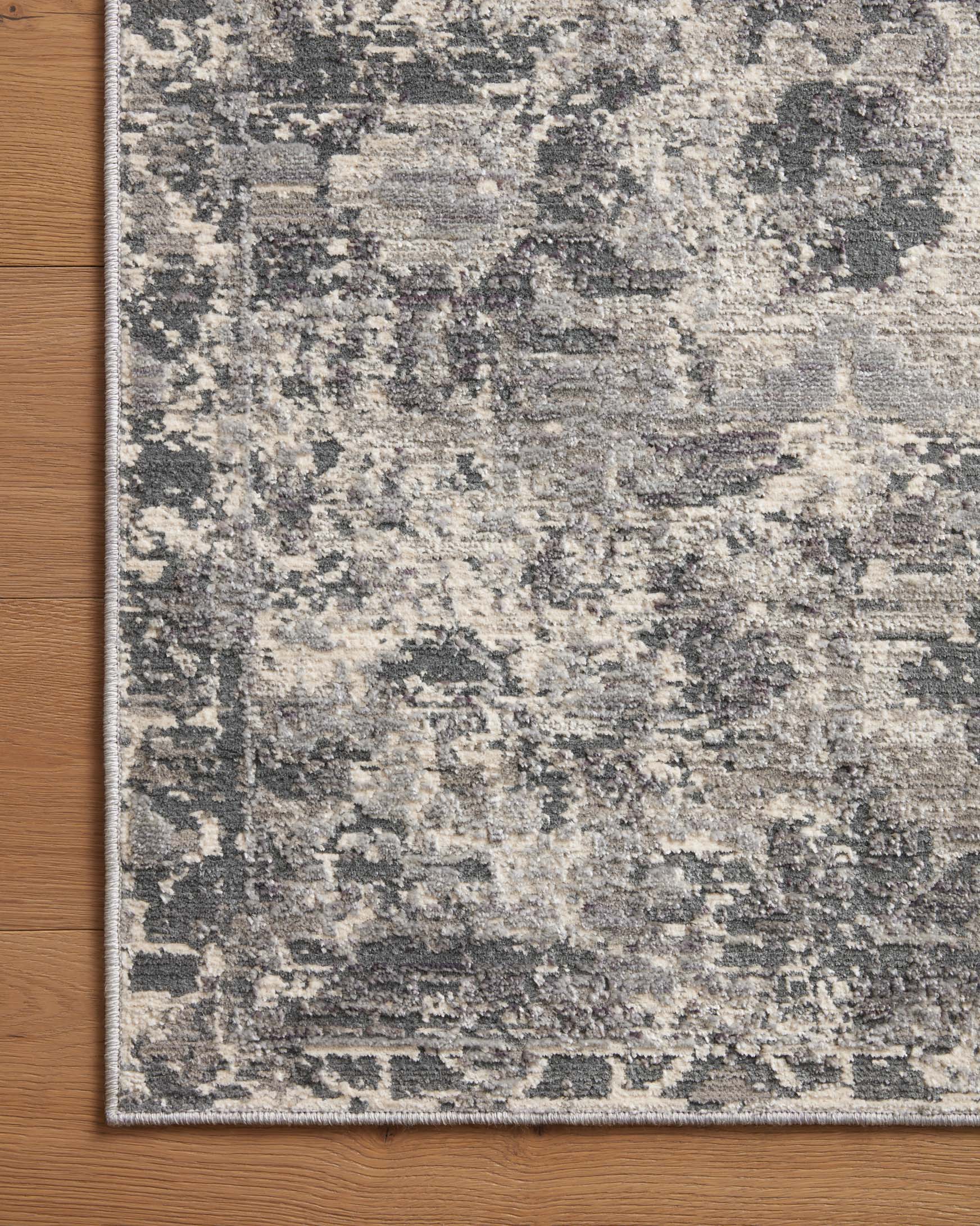 Charcoal and silver area rug corner detail with abstract distressed pattern and border trim.