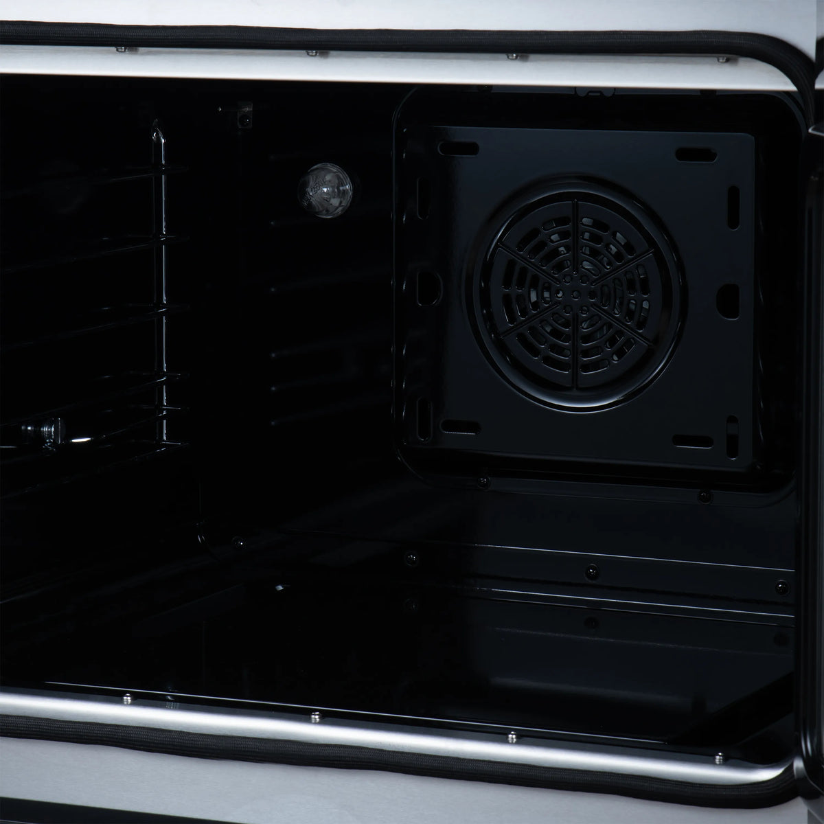 Open black oven cavity with rack supports and round convection fan cover on back wall