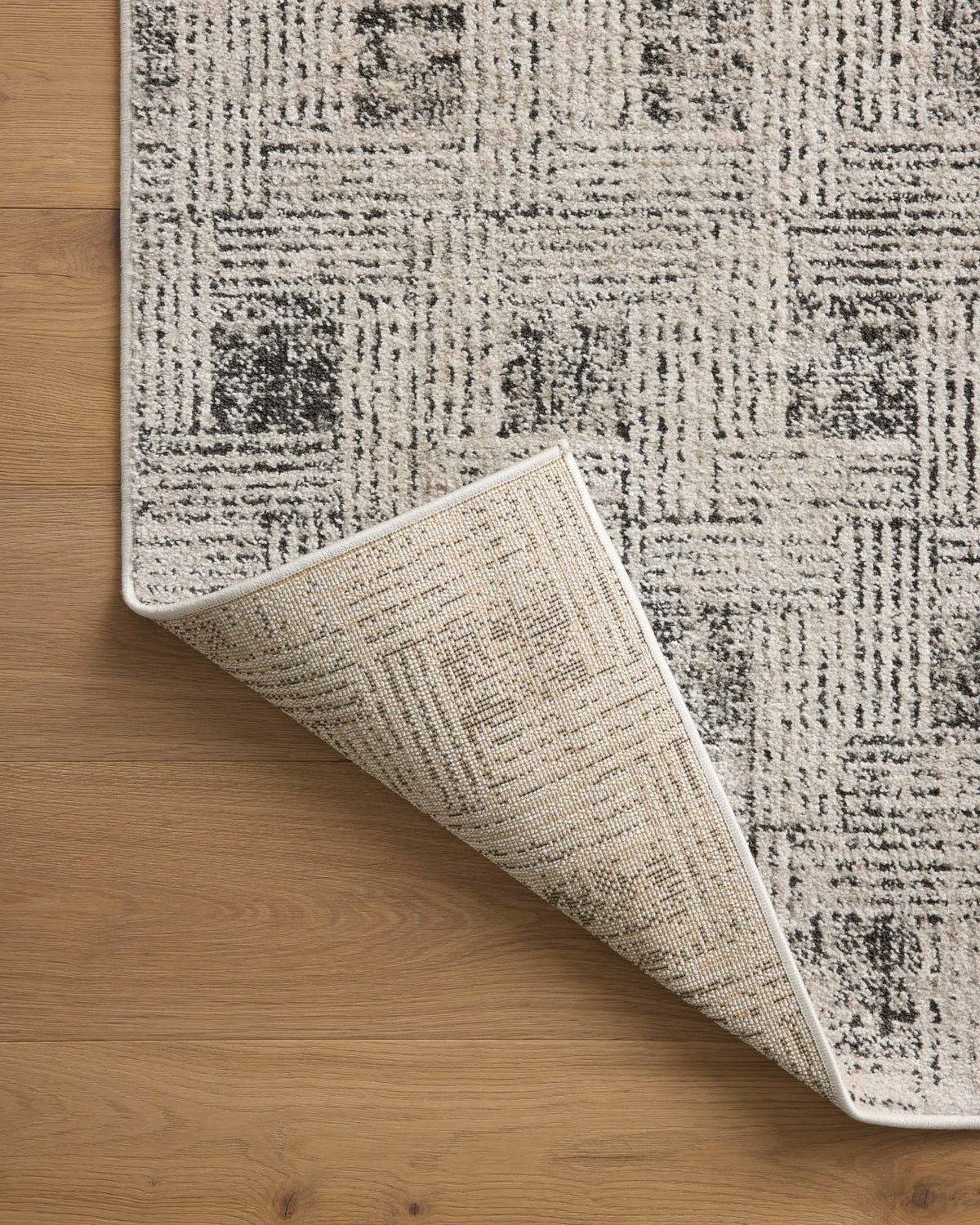 Grey and graphite rug rolled corner detail, textured flat weave on wood floor.