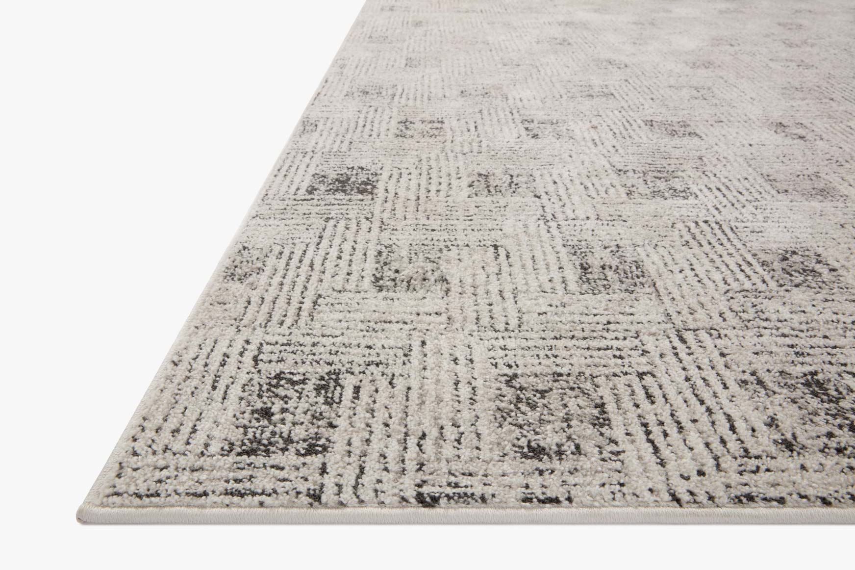 Grey accent rug corner view with textured abstract lines and dark speckles.