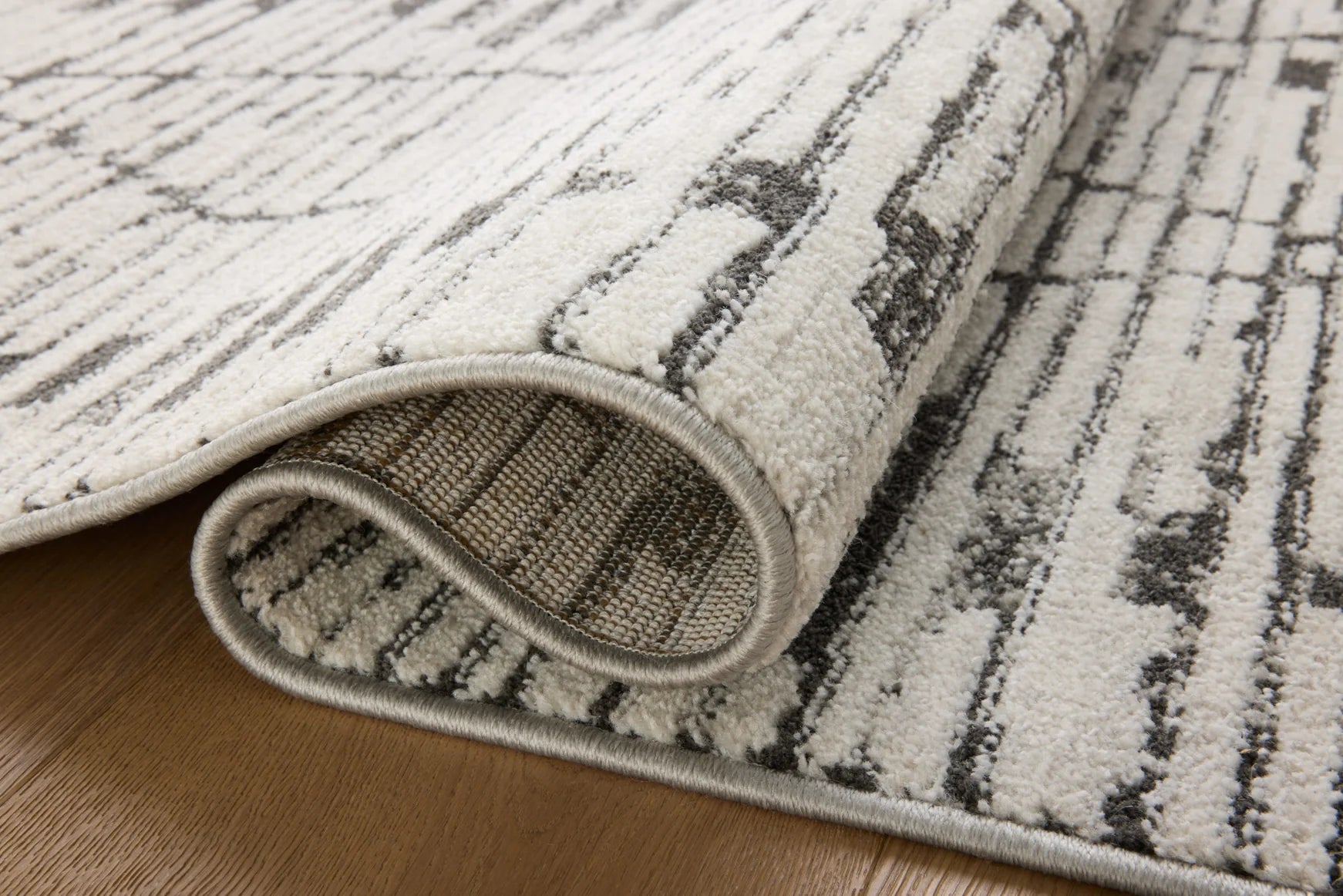 Corner detail of charcoal and dove area rug with textured pile and curved edge