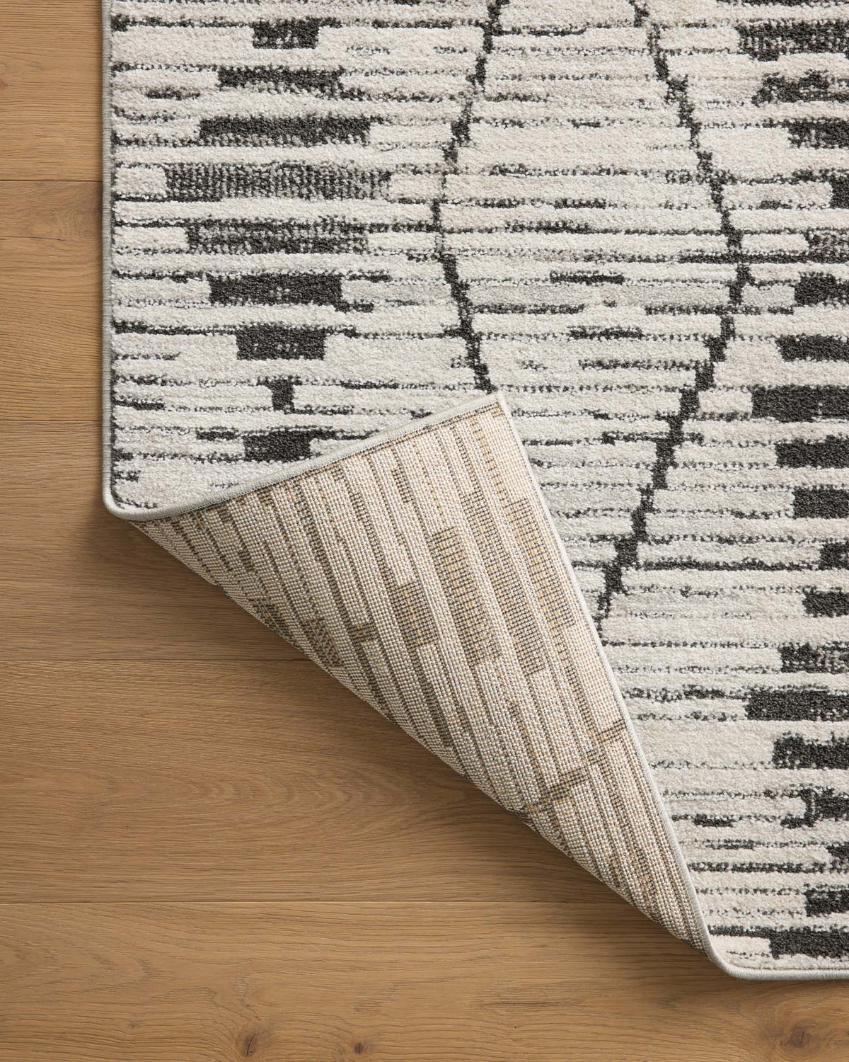 Area rug corner curling to show underside lining in off-white and tan