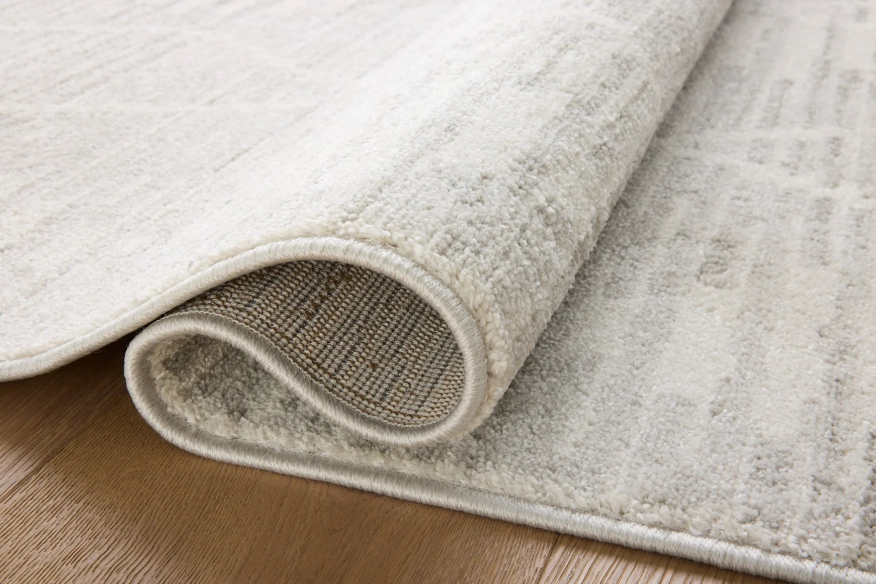 Ivory and silver area rug rolled edge, showing low-pile texture and border trim.