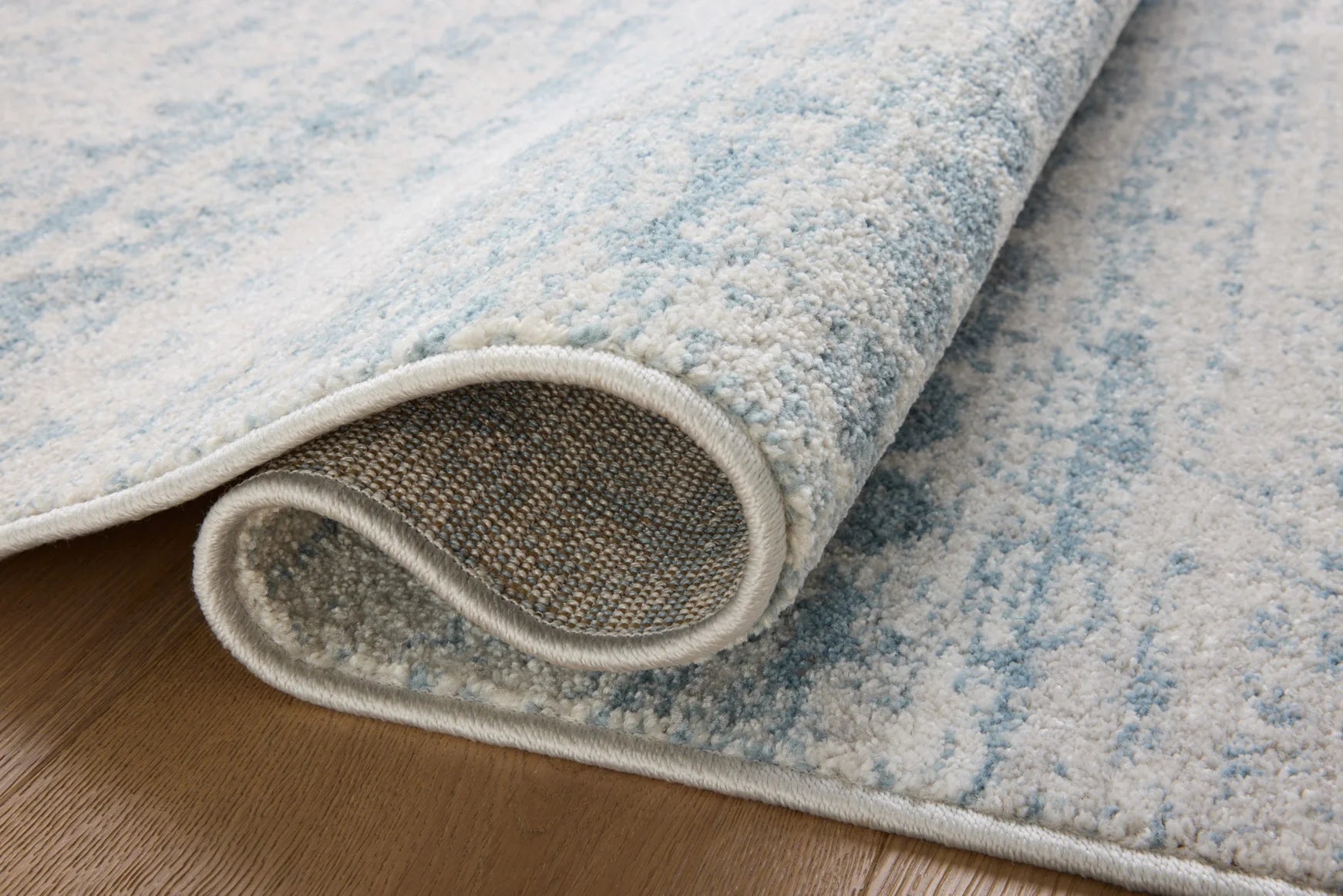 Rug corner with light gray binding and sky-and-dove abstract texture from the edge