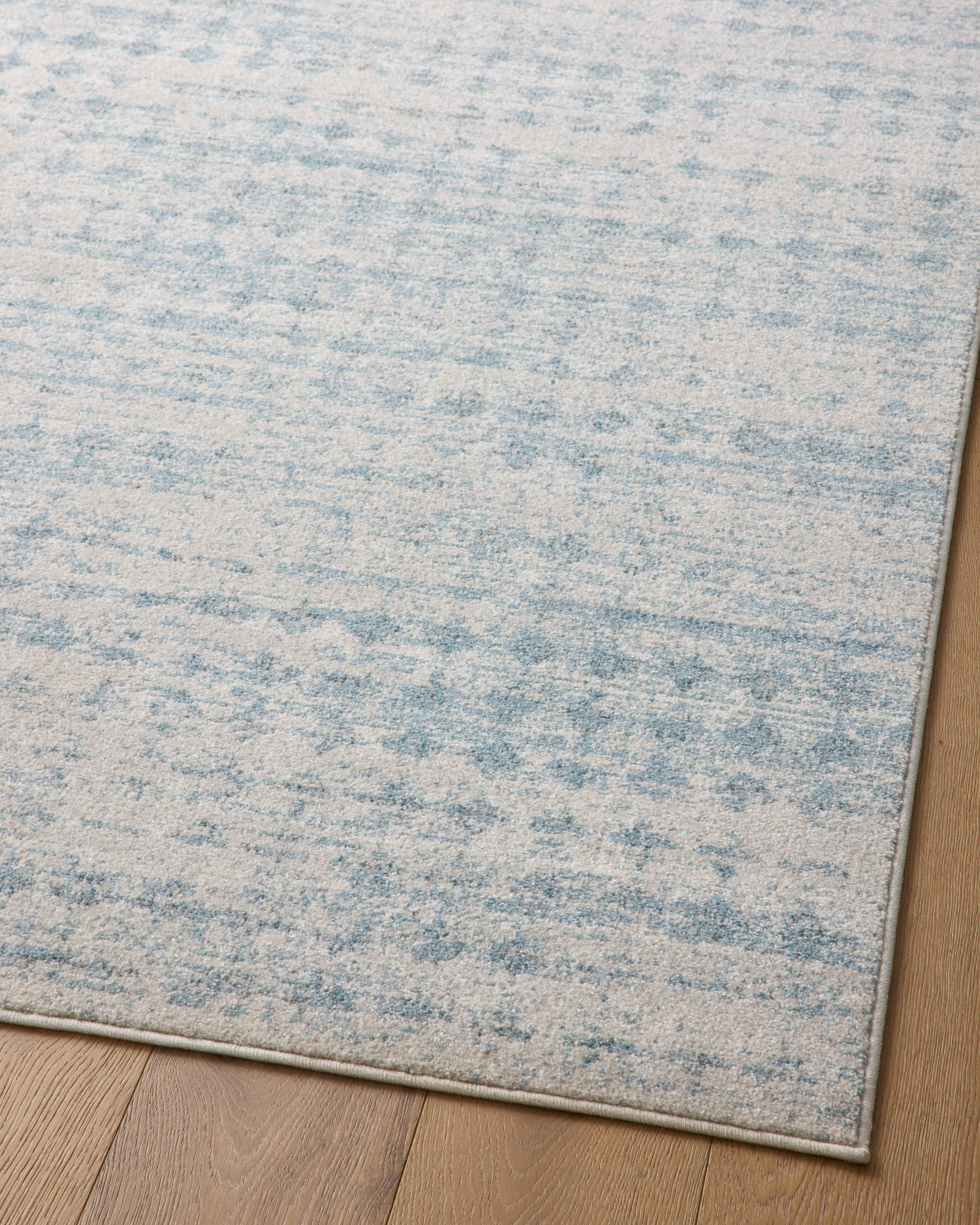 Light blue area rug with dove-toned speckled texture, laid flat on wood flooring