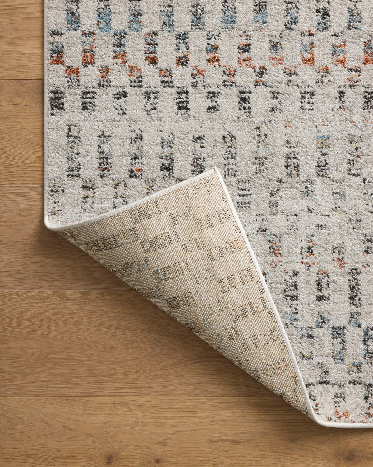 Grey rug partially lifted on wood floor, revealing underside and low-pile texture