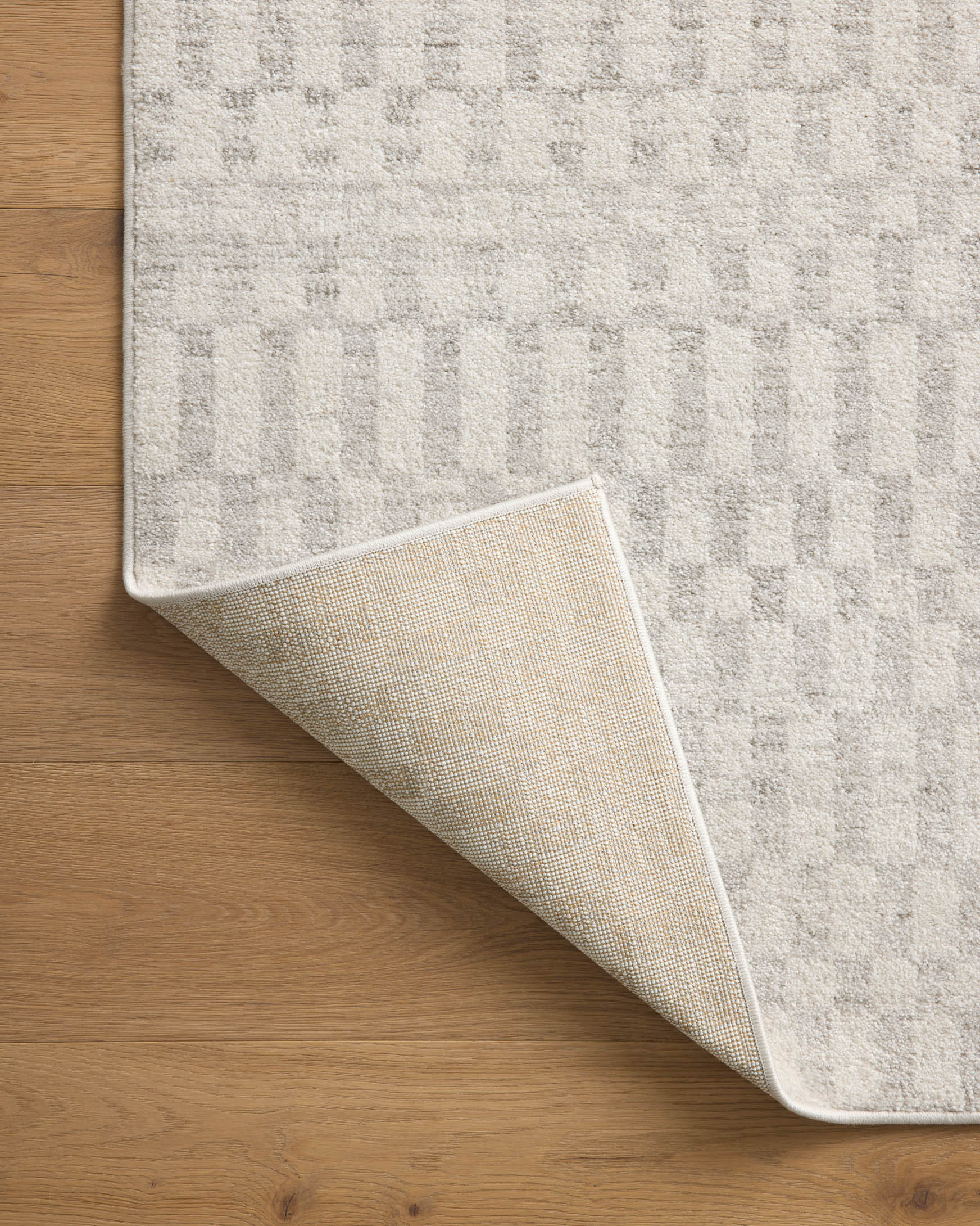 Ivory and grey rug corner lifted, showing textured backing and edge binding