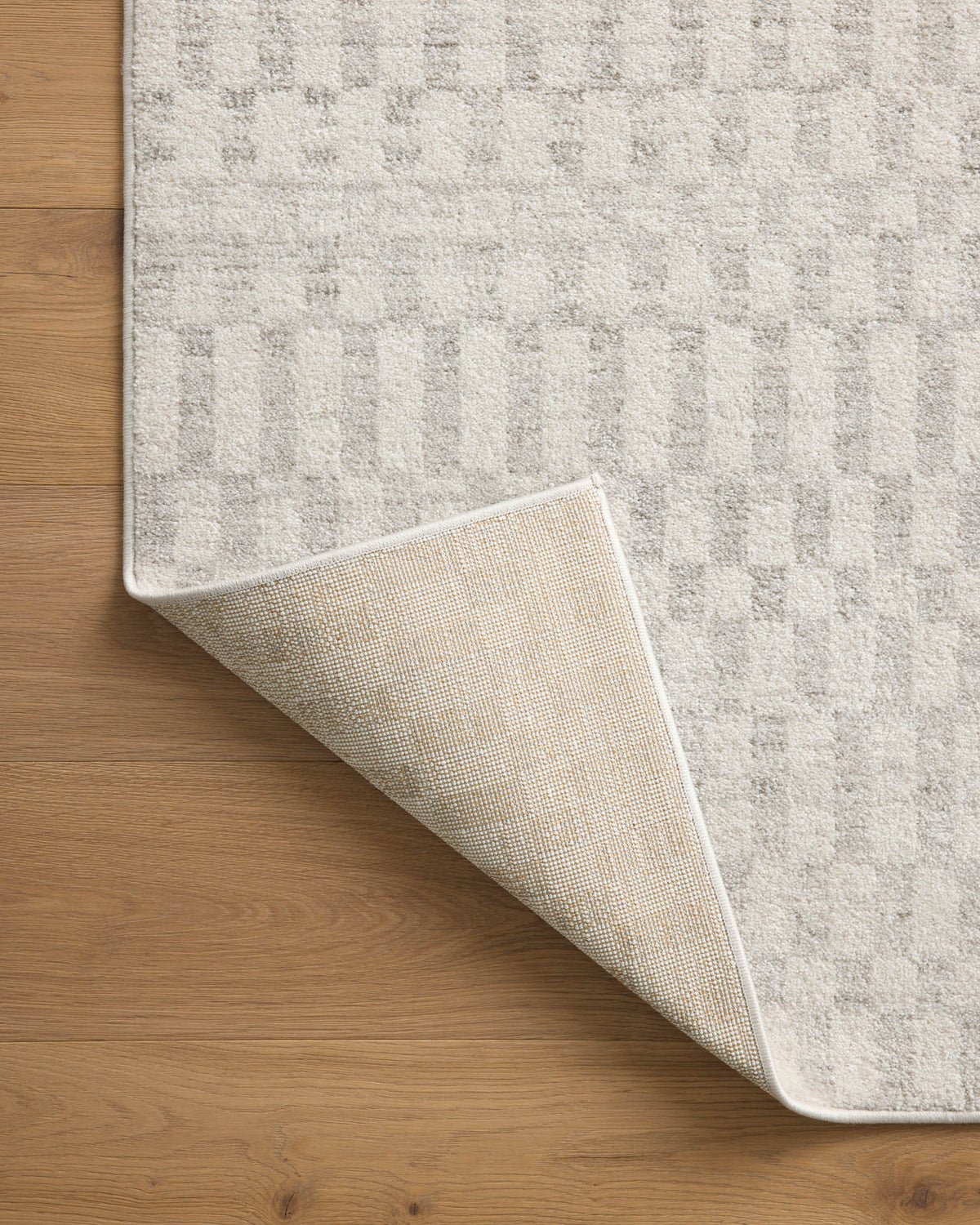 Ivory and light gray area rug showing underside backing when corner is lifted.