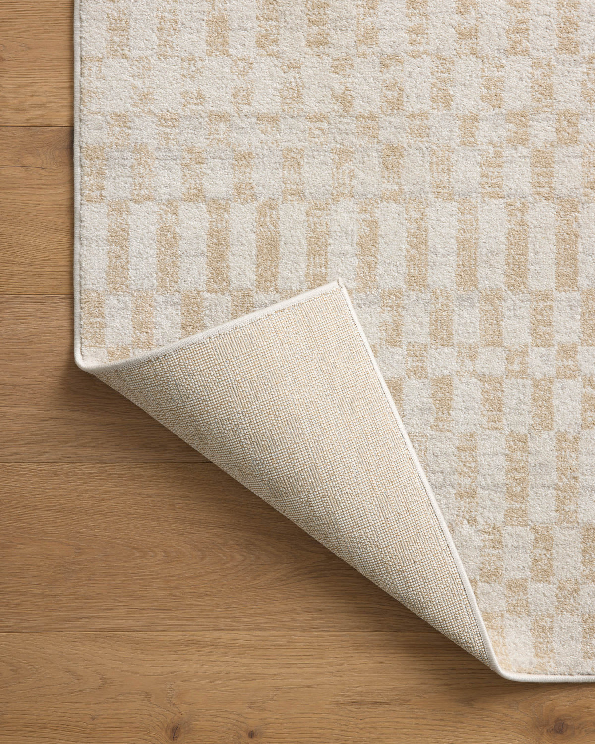 Ivory checker-pattern area rug corner folded back on wood floor