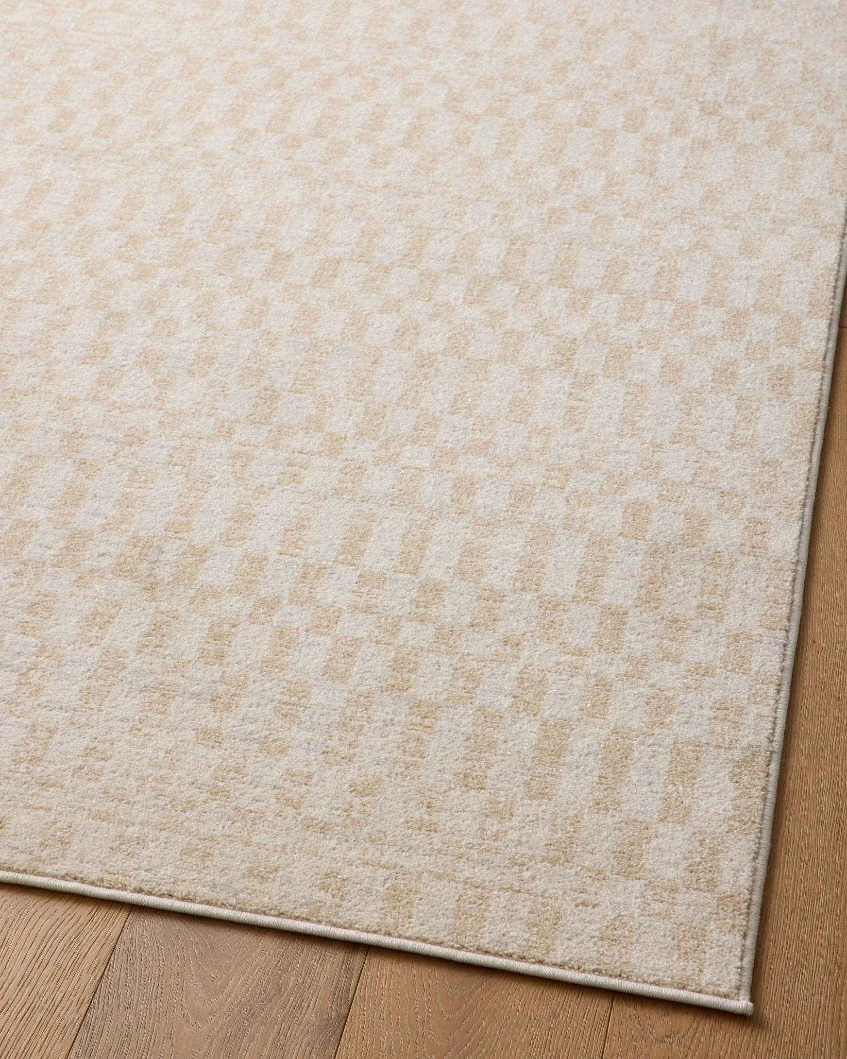 Ivory area rug with small check pattern and low-pile texture on wood floor.