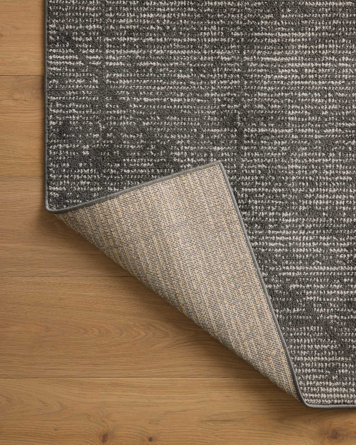 Charcoal runner rug edge rolled upward to show underside, ivory and charcoal woven texture