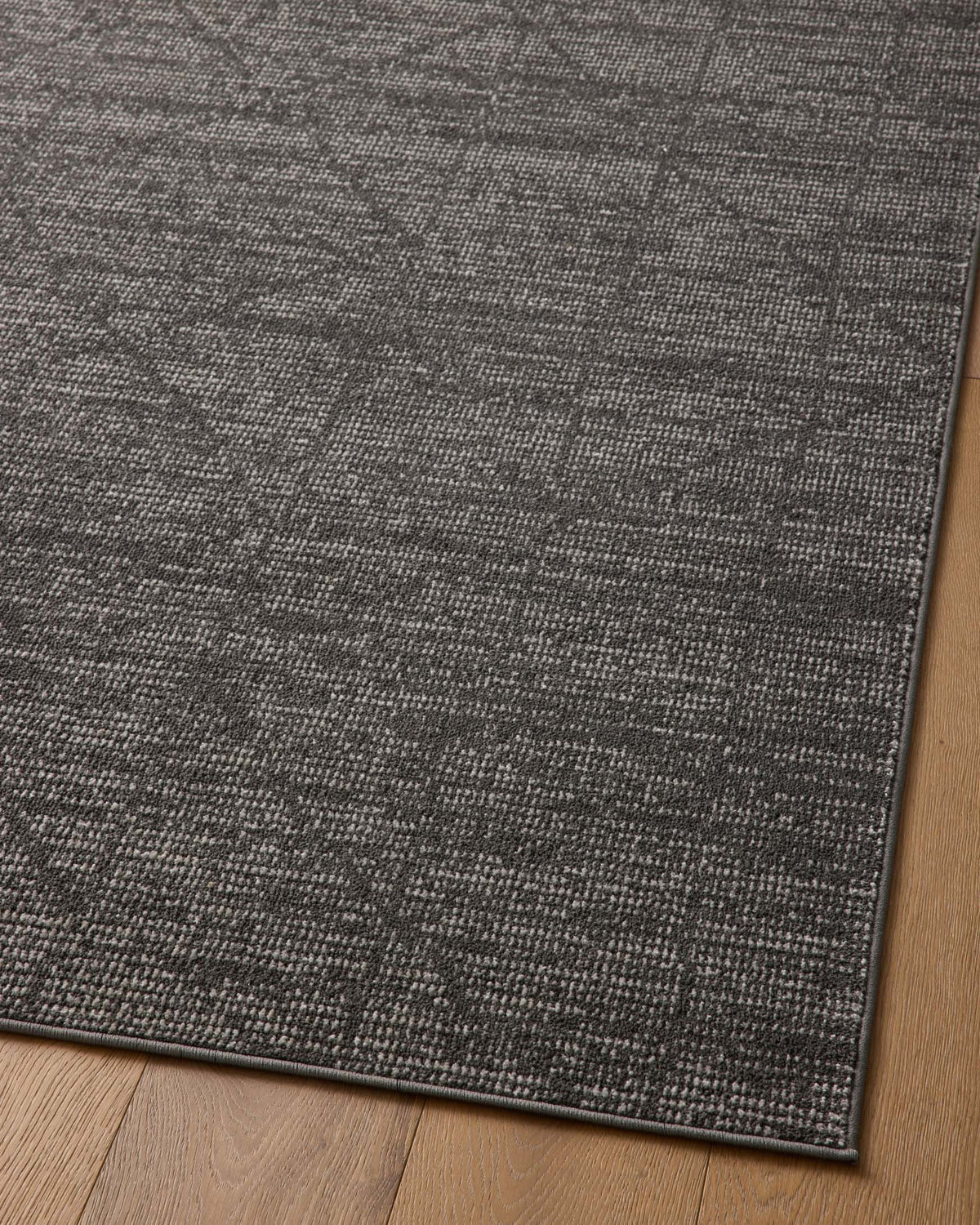 Charcoal-and-ivory area rug corner with distressed geometric pattern and bound edge
