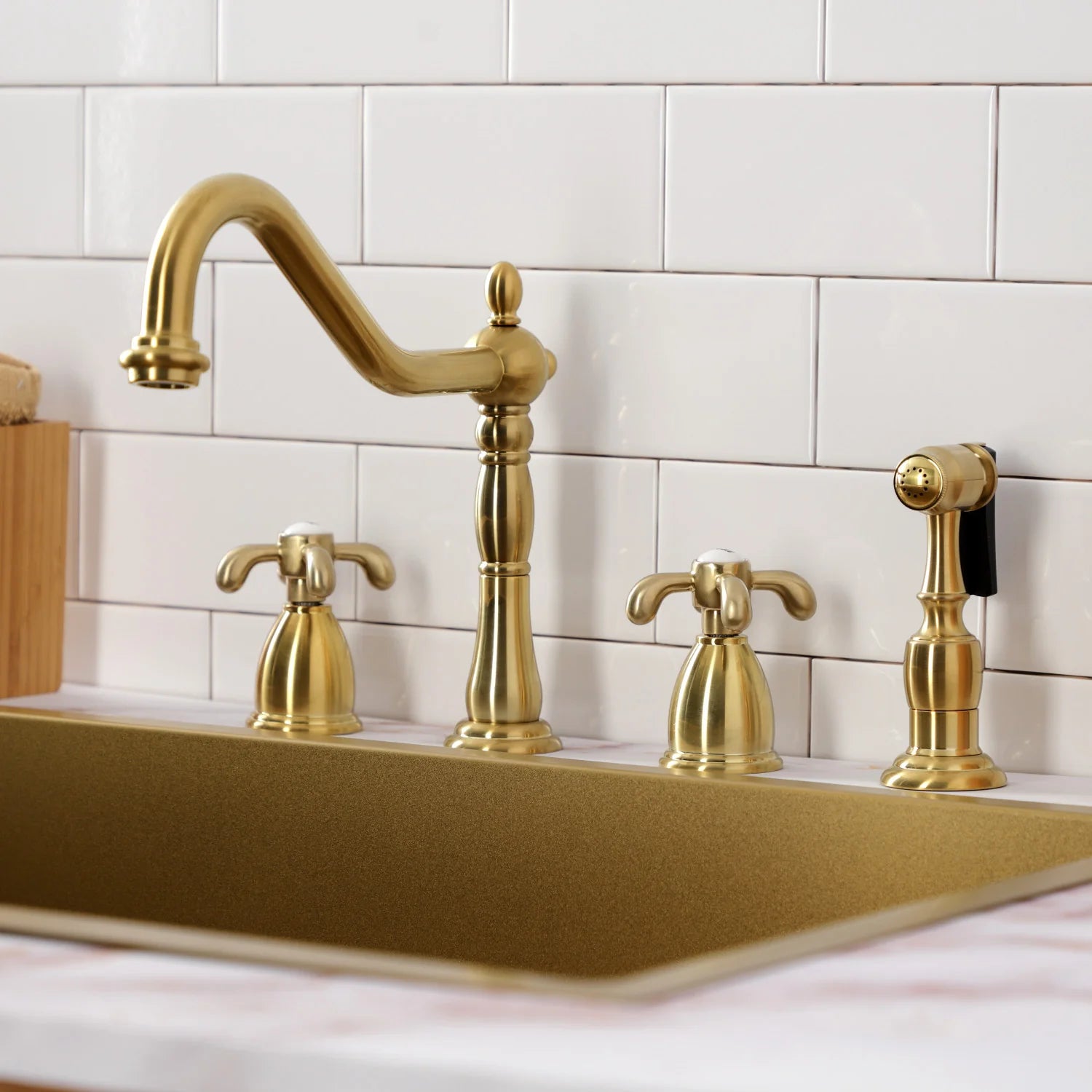 Brushed brass kitchen faucet with arch spout and matching sprayer on countertop