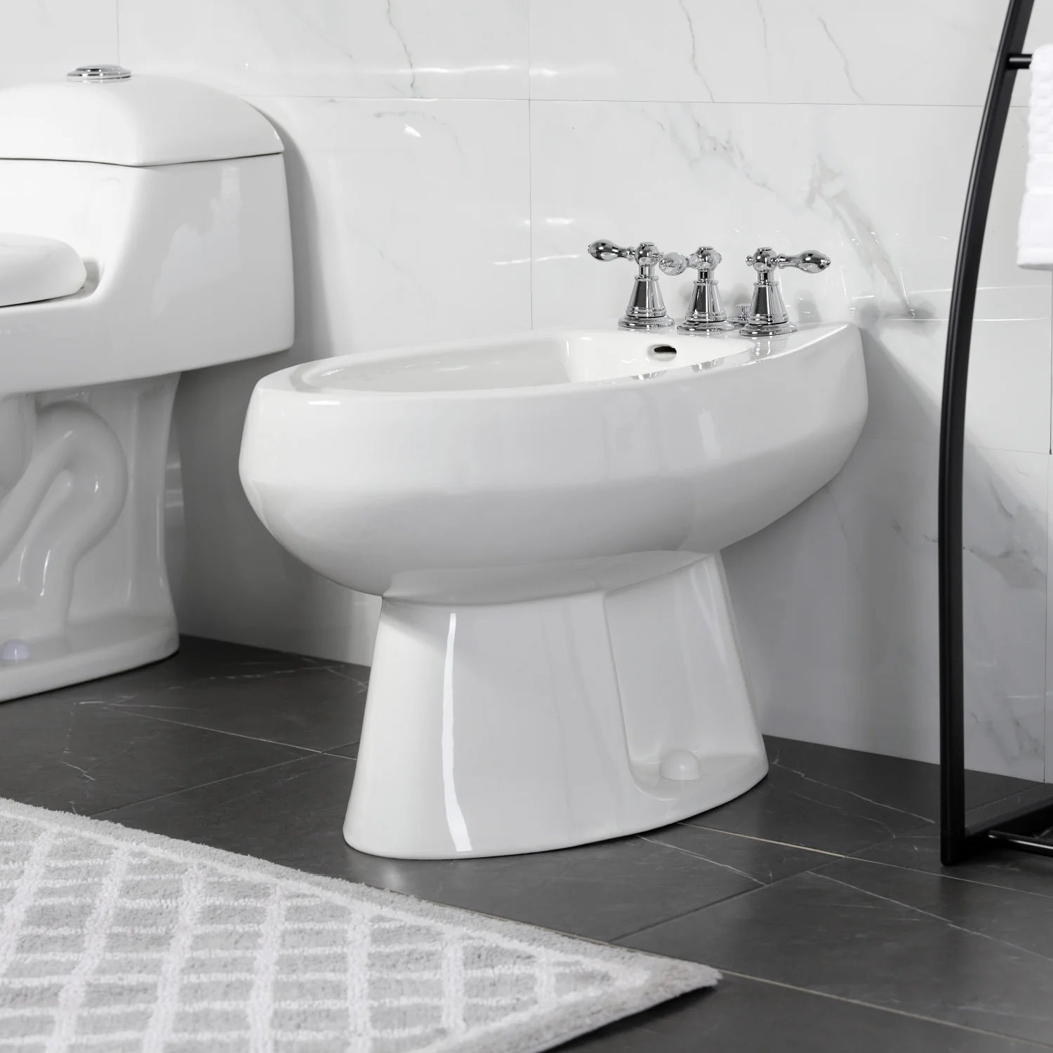Polished chrome three-handle bidet faucet on white bidet in bathroom setting