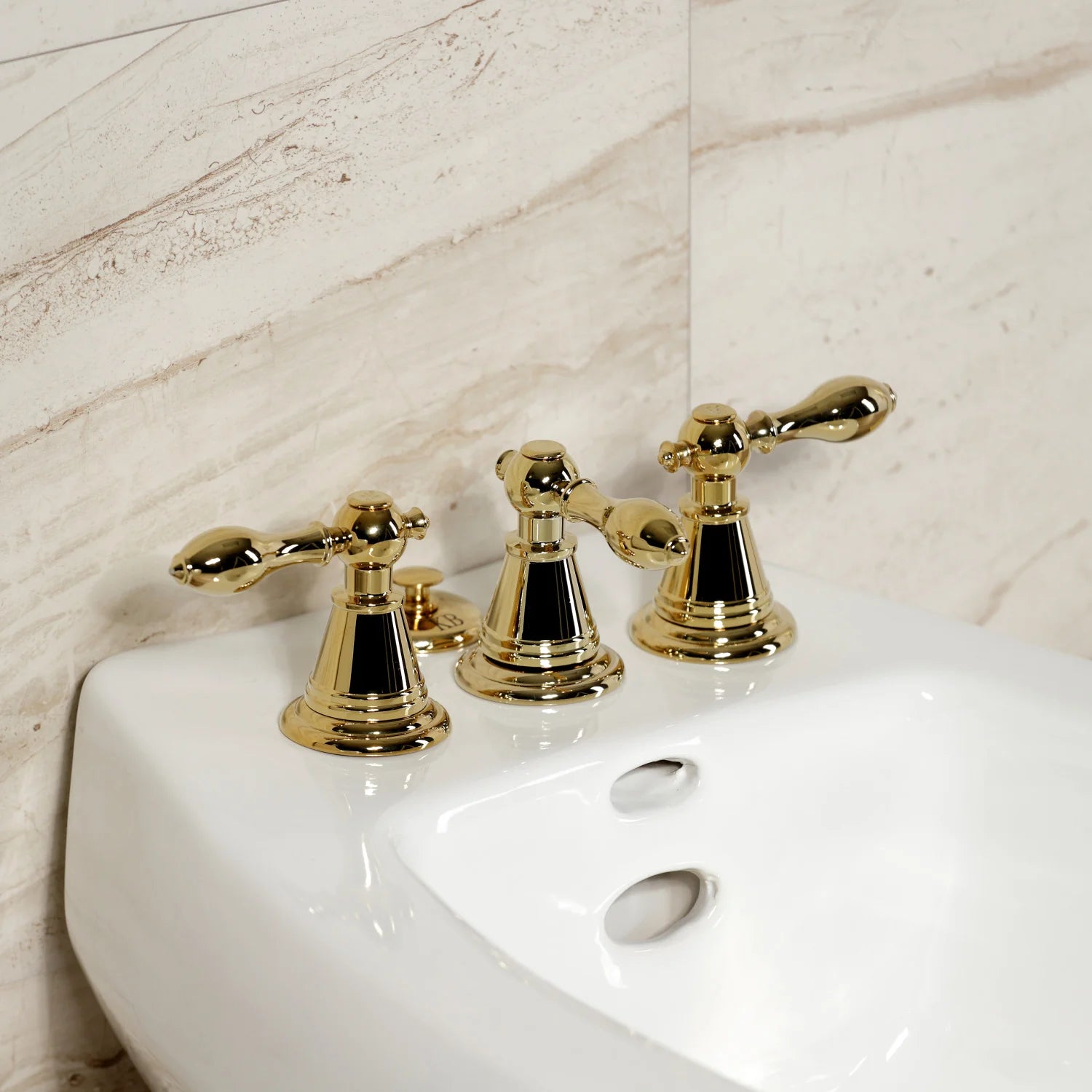 Polished brass three-handle bidet faucet mounted on a white bidet basin