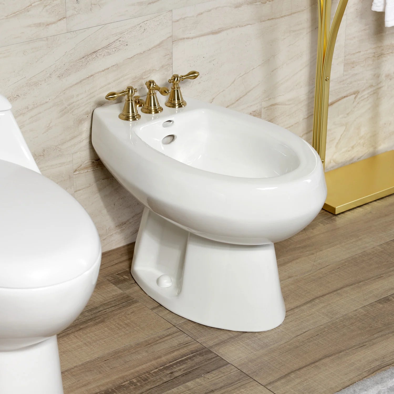 Brushed brass three-handle bidet faucet with curved spout on white pedestal bidet