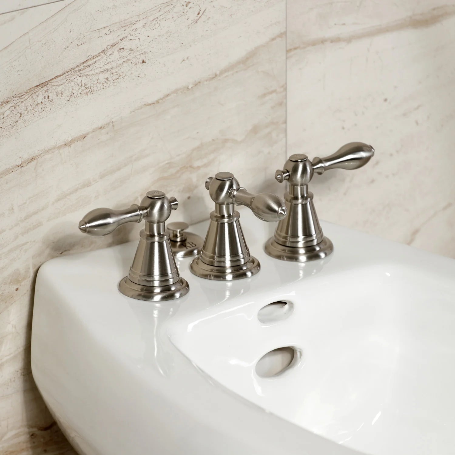 Brushed nickel three-handle bidet faucet with ornate spouts and handles.
