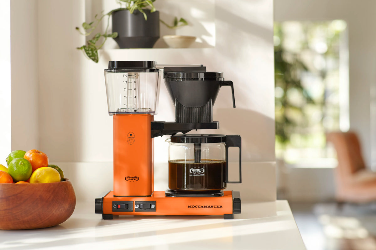 Orange coffee maker on countertop with clear water tank, black components, and glass carafe