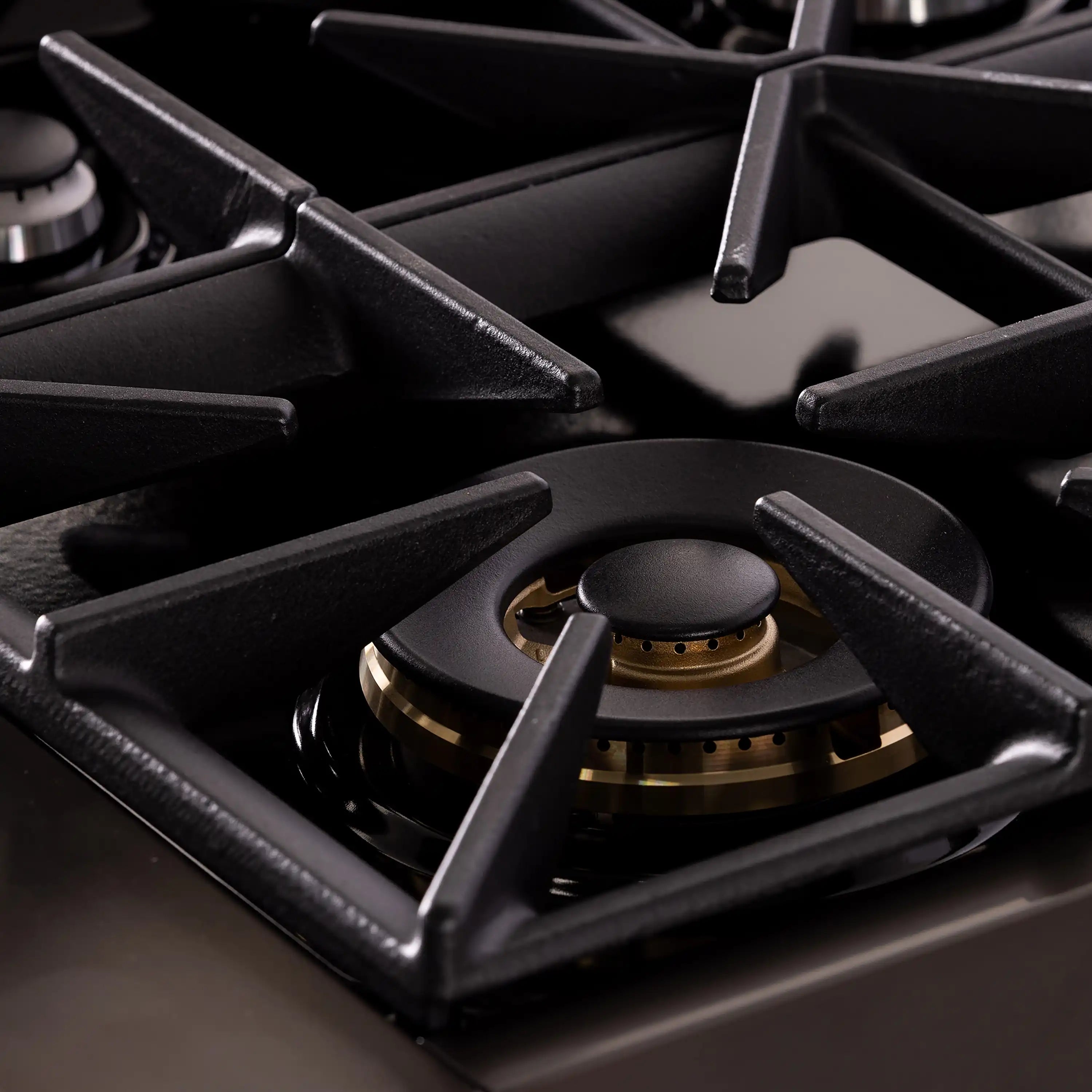 Gas range burner grate with gold-ring control knob on dark cooktop