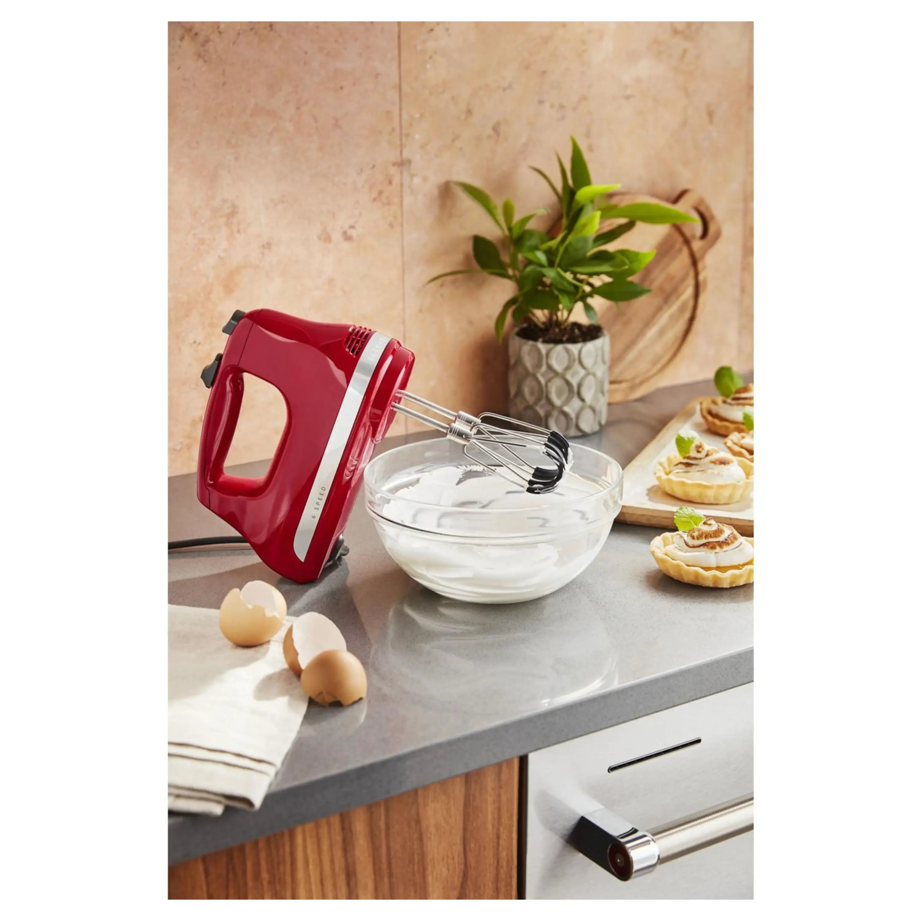 Red hand mixer with metal beaters, shown over a mixing bowl