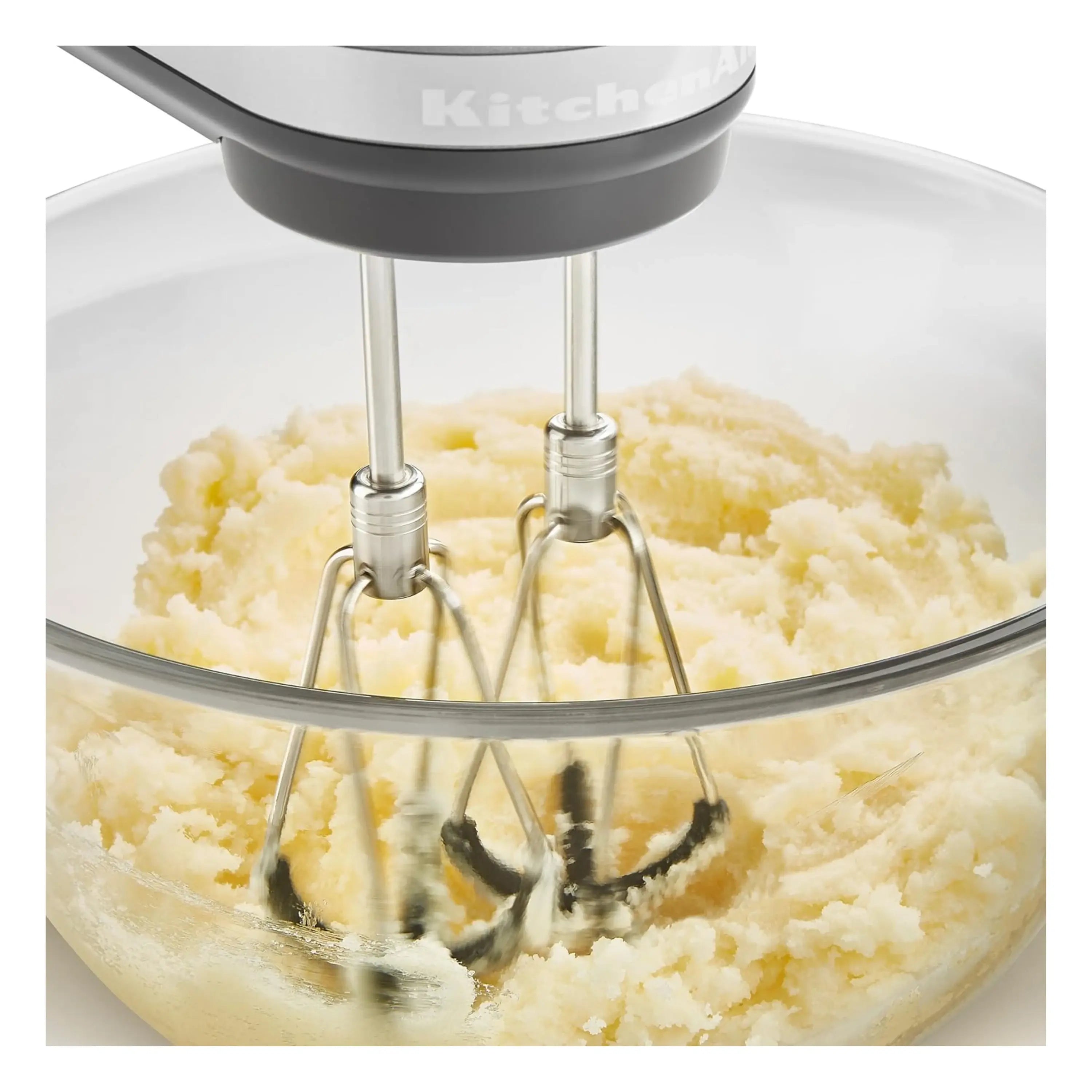 Red hand mixer beaters churning batter in a glass mixing bowl