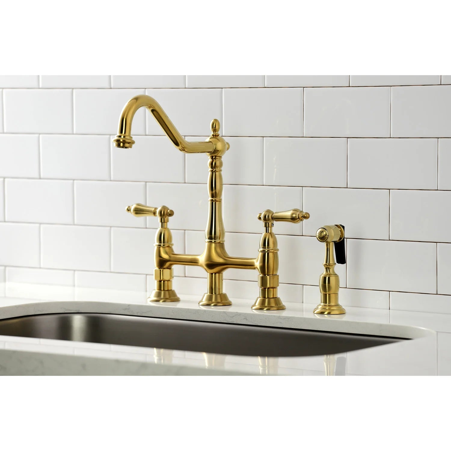 Brushed brass kitchen faucet and sprayer on sink deck against white tile