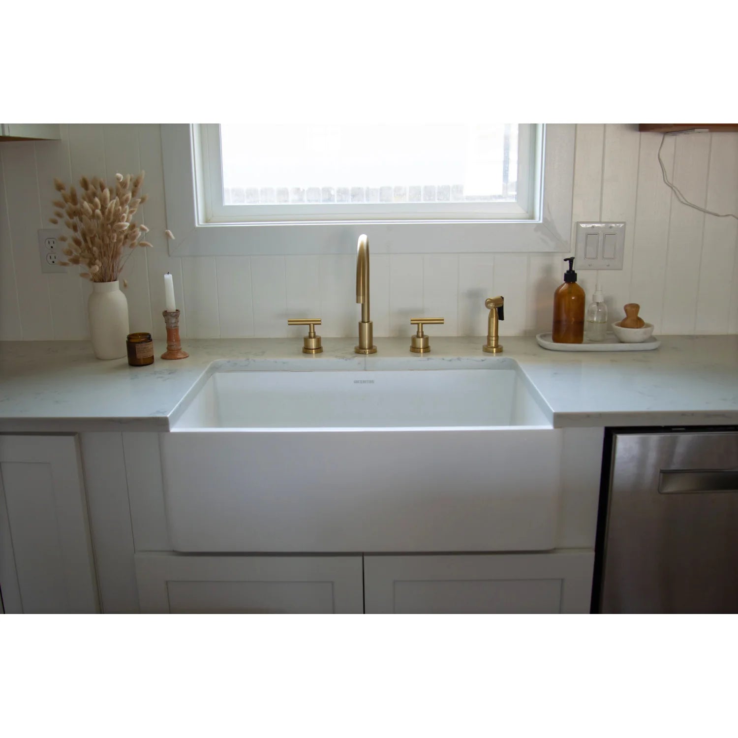 Brushed brass widespread faucet with two handles centered over farmhouse sink