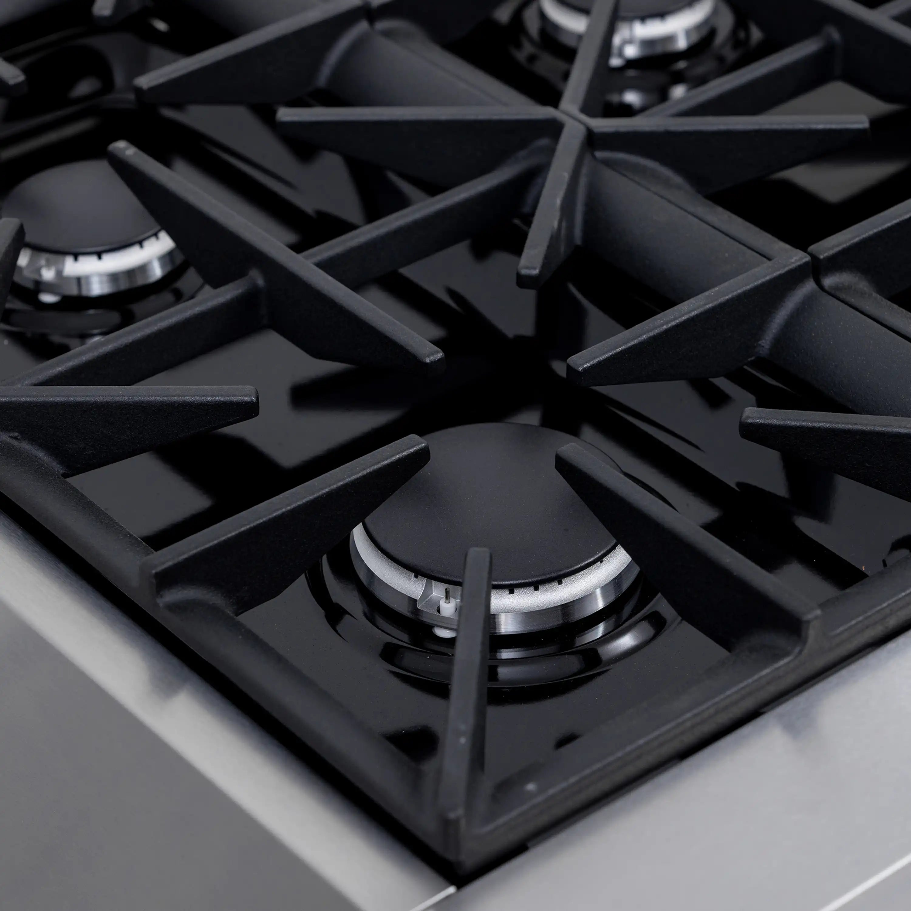 Gas burner grate with black burner heads on a stainless dual fuel range cooktop