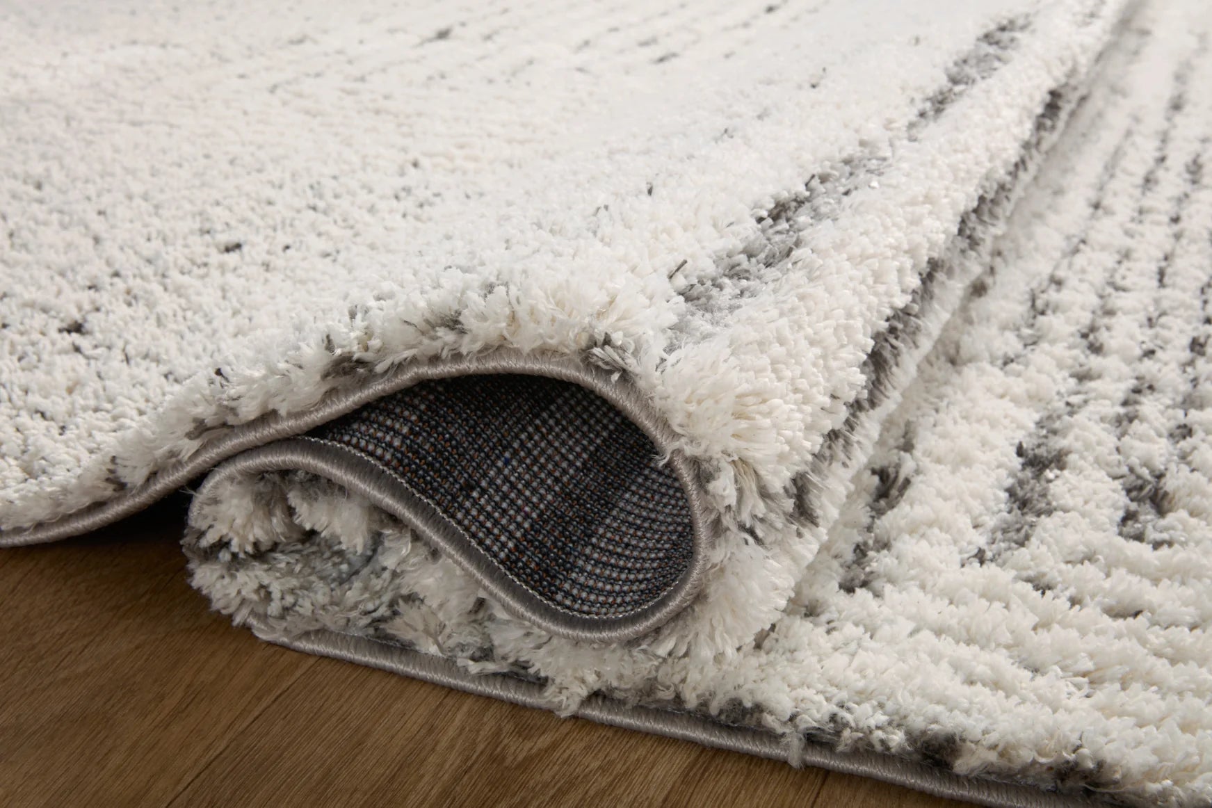 Ivory shag area rug edge with grey underside backing and looped pile texture