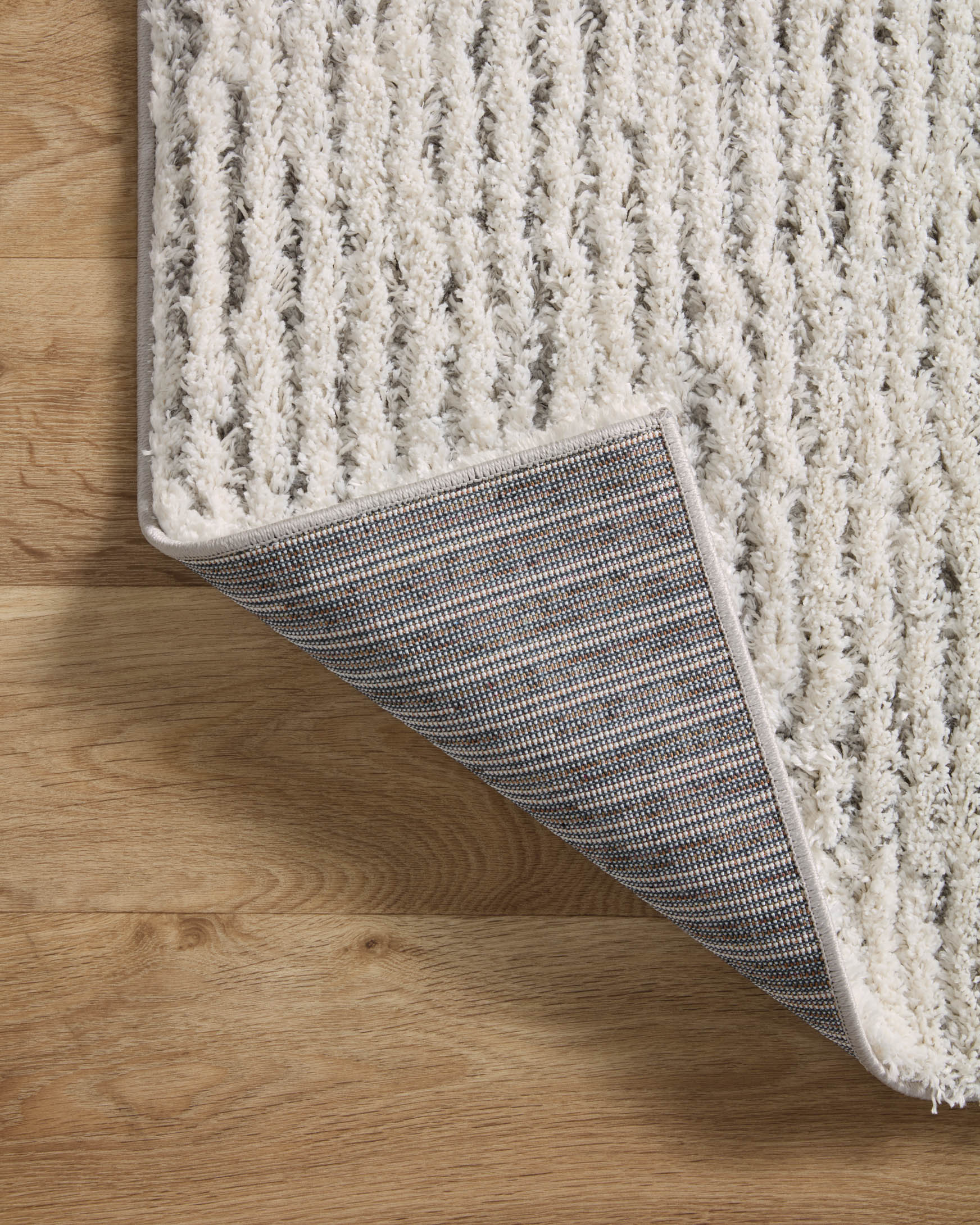 Shag rug corner showing grey woven underside and stitched edge