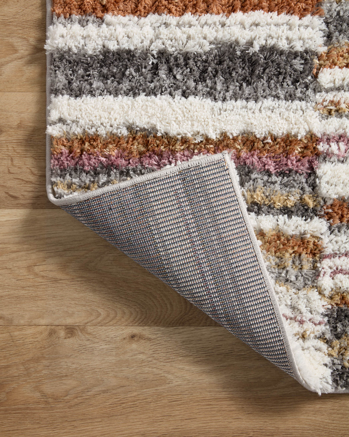 Shag area rug with multicolor stripes and gray woven backing at corner