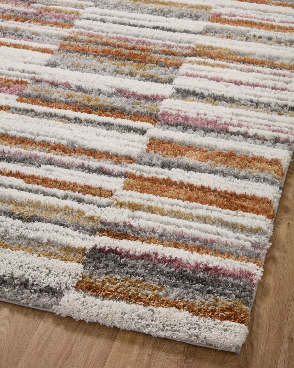 View of striped shag runner rug showing dense pile in ivory, gray, orange, and rose hues
