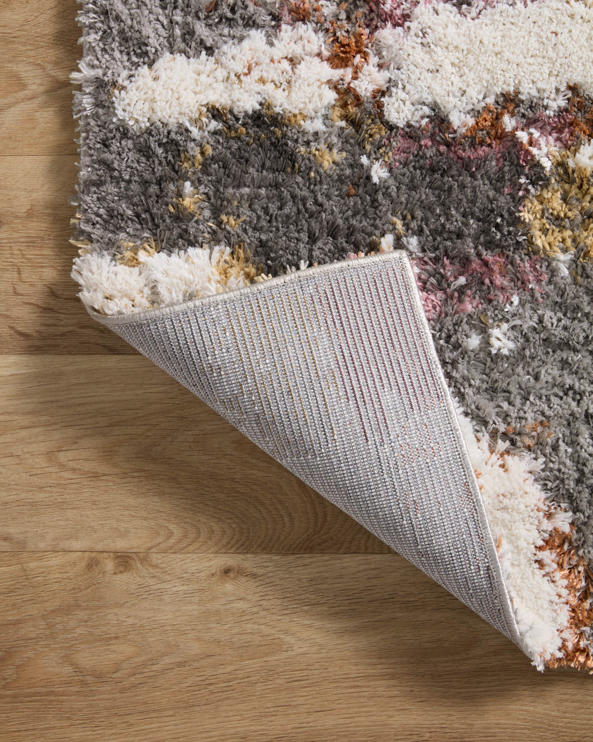 Folded grey shag rug showing cream top and textured grey backing along edge.