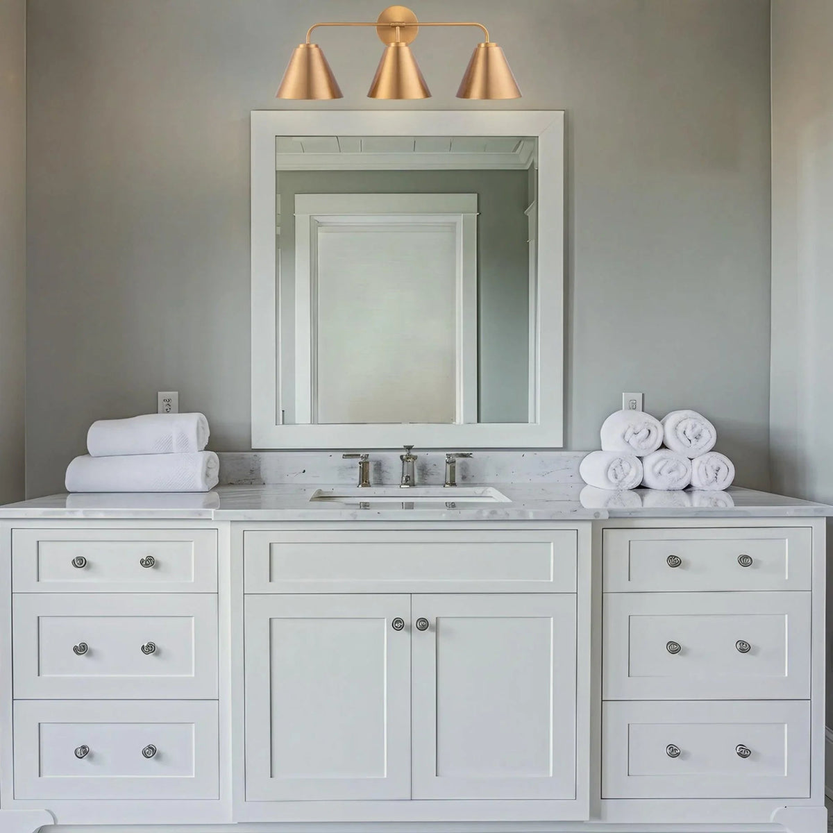 Golden 3-light vanity light with three cone shades over a white vanity setup