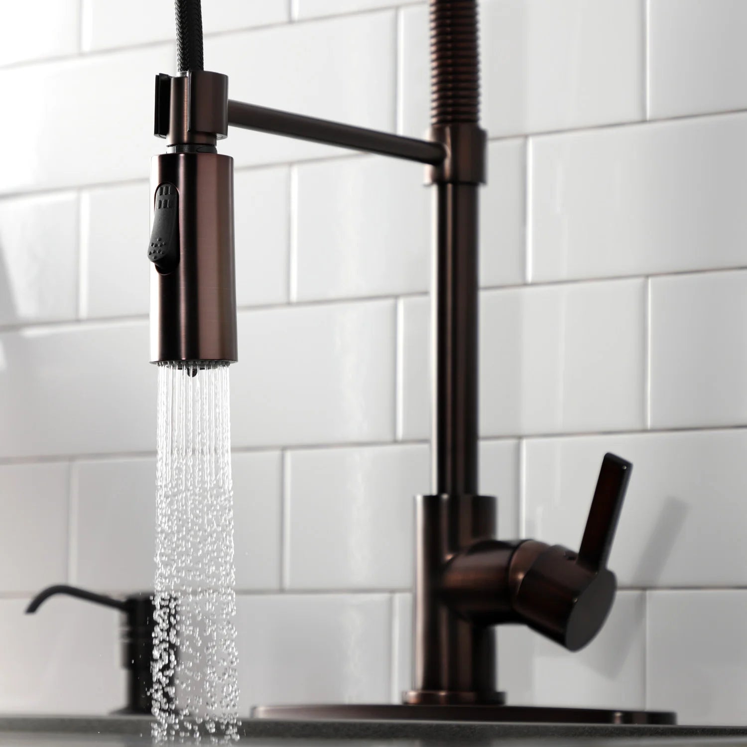 Oil-rubbed bronze kitchen faucet dispensing water from the pull-down spray head
