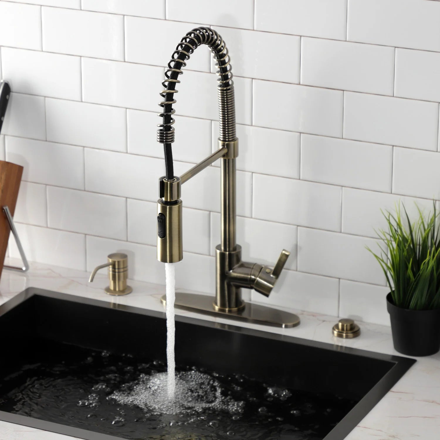 Antique brass deck-mount pre-rinse faucet with arched spray hose above black sink