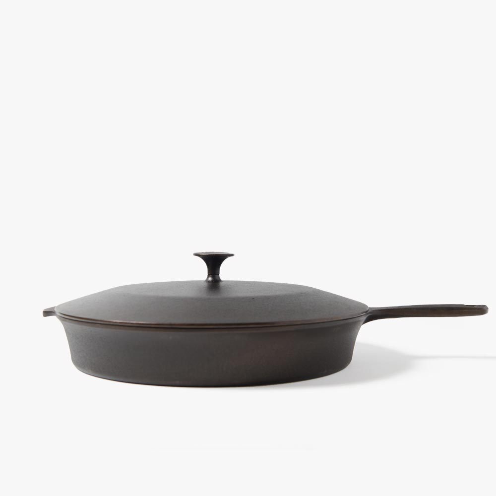 Dark cast iron skillet with matching lid, central knob, and side handle