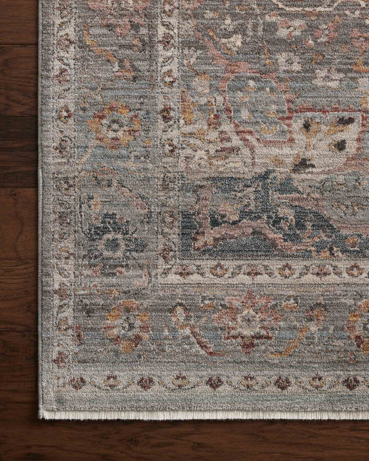 Distressed area rug close-up with gray-blue field, faded motifs, and fringed edge